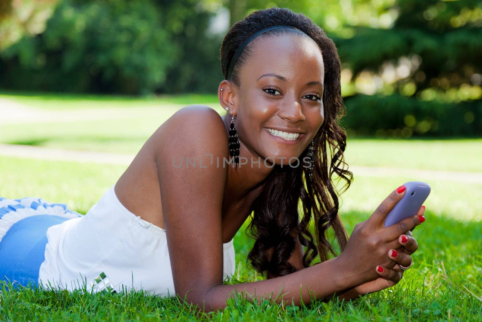 Smiling teenage black girl using a phone, lying on the grass