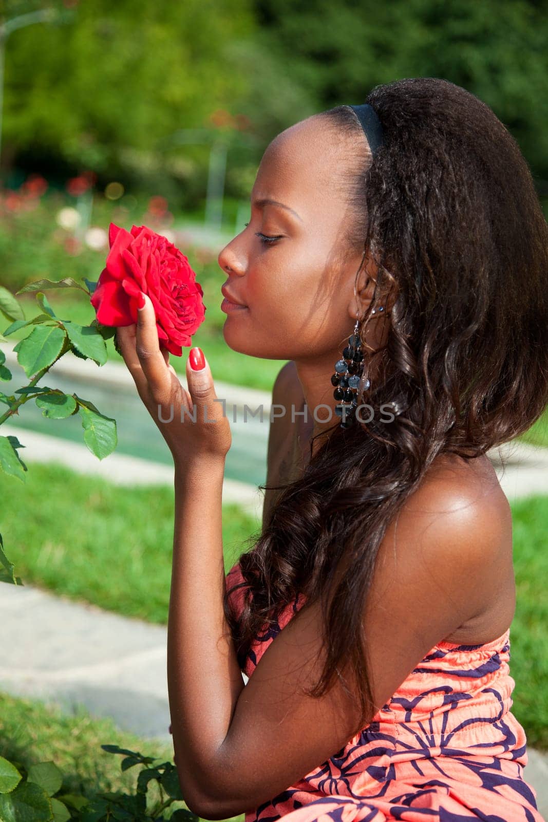 Outdoor portrait of a young beautiful african american girl smelling flowers