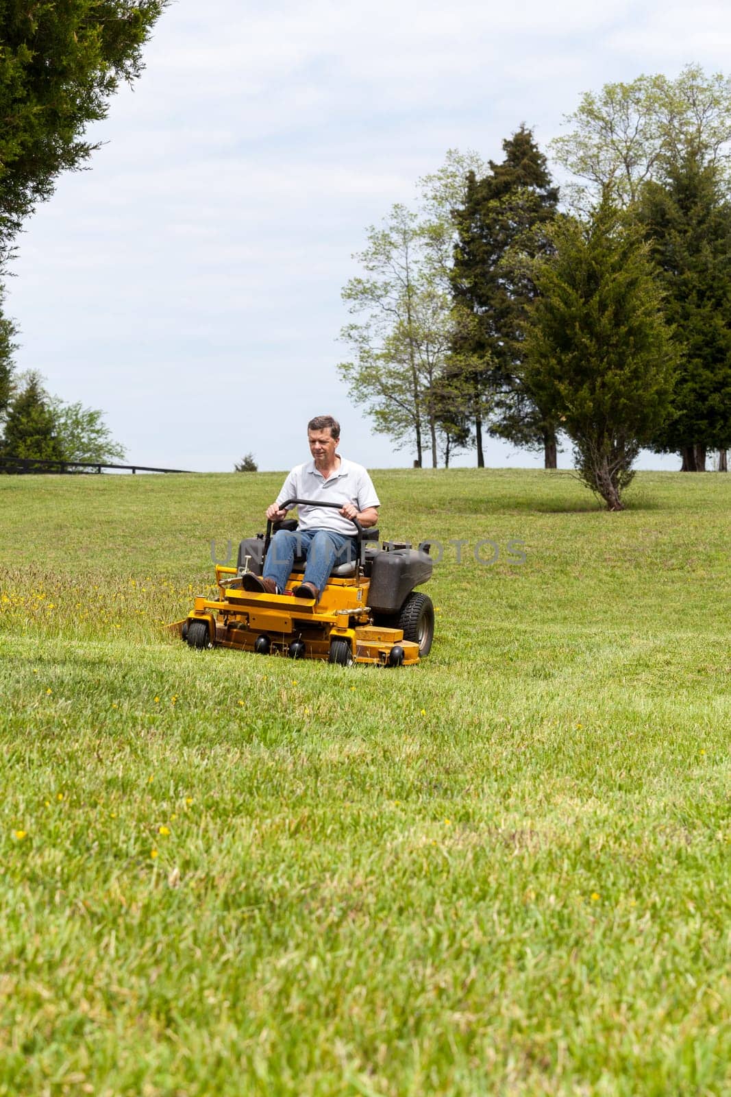 Senior retired male cutting the grass on expansive lawn using yellow zero-turn mower