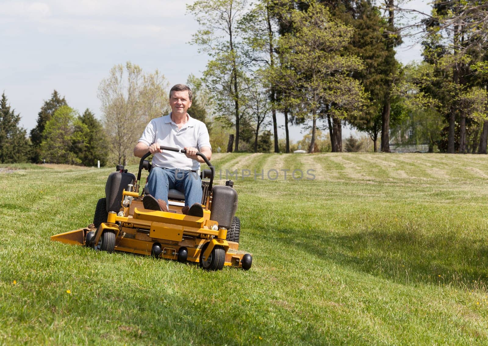 Senior retired male cutting the grass on expansive lawn using yellow zero-turn mower