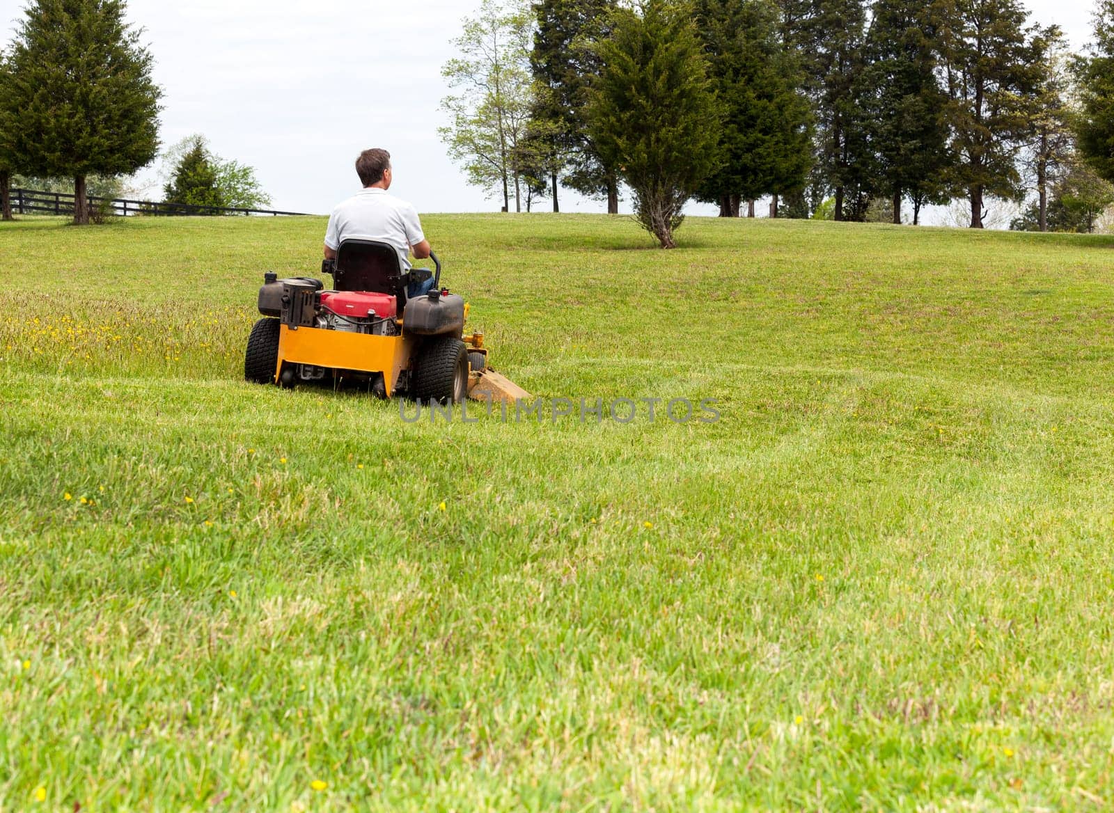 Senior retired male cutting the grass on expansive lawn using yellow zero-turn mower