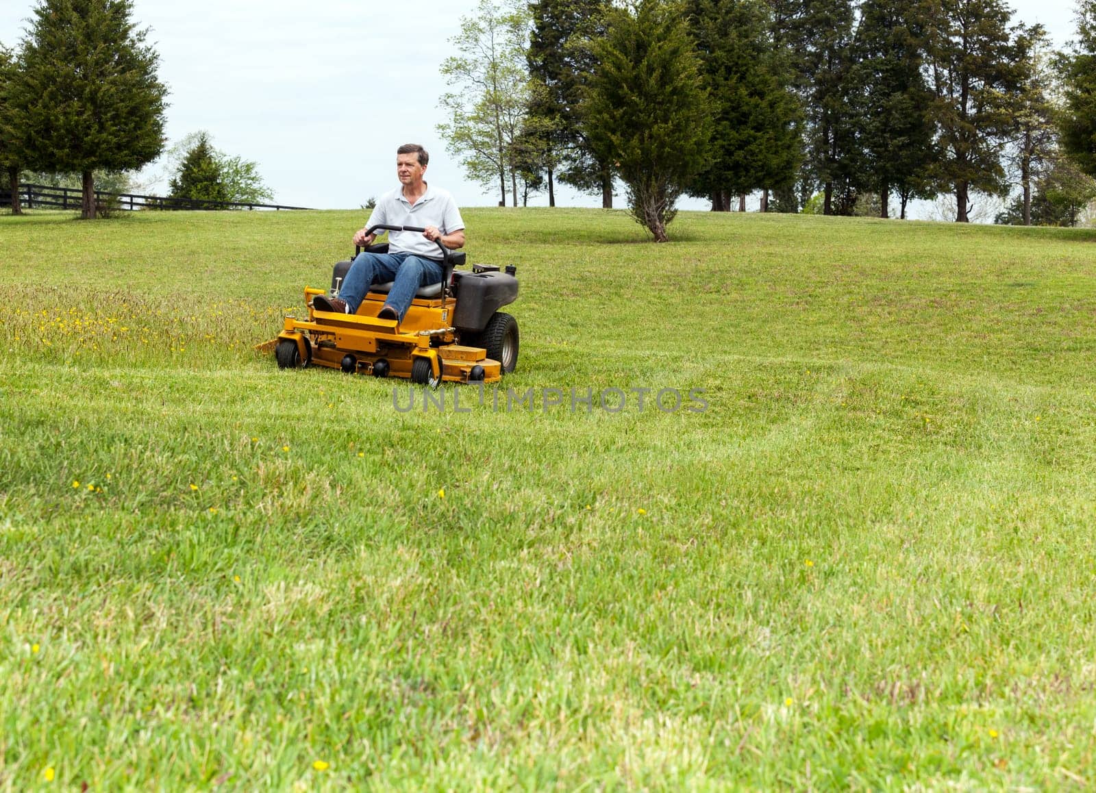 Senior retired male cutting the grass on expansive lawn using yellow zero-turn mower