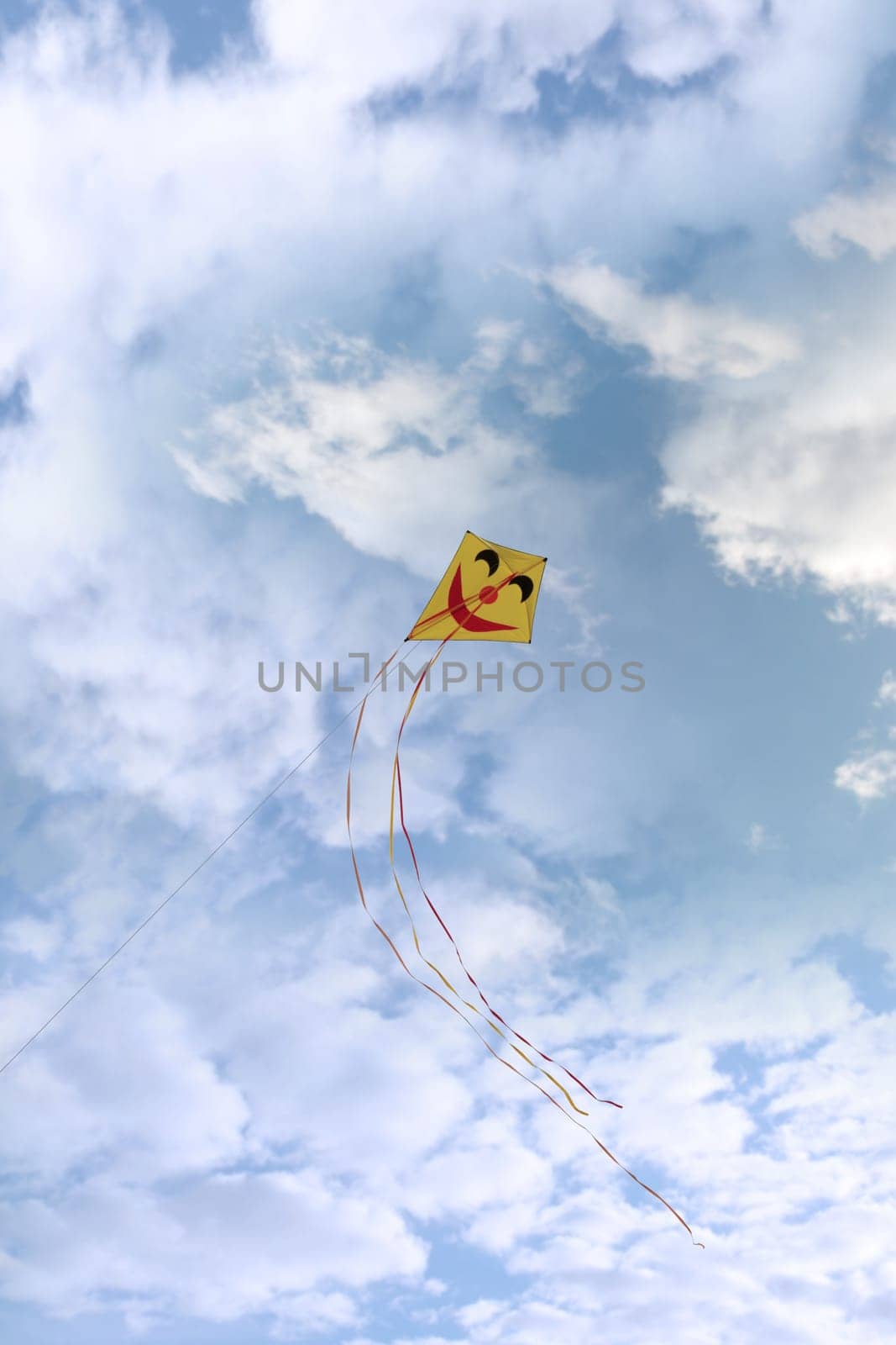 a smiley kite high in the cloudy blue sky