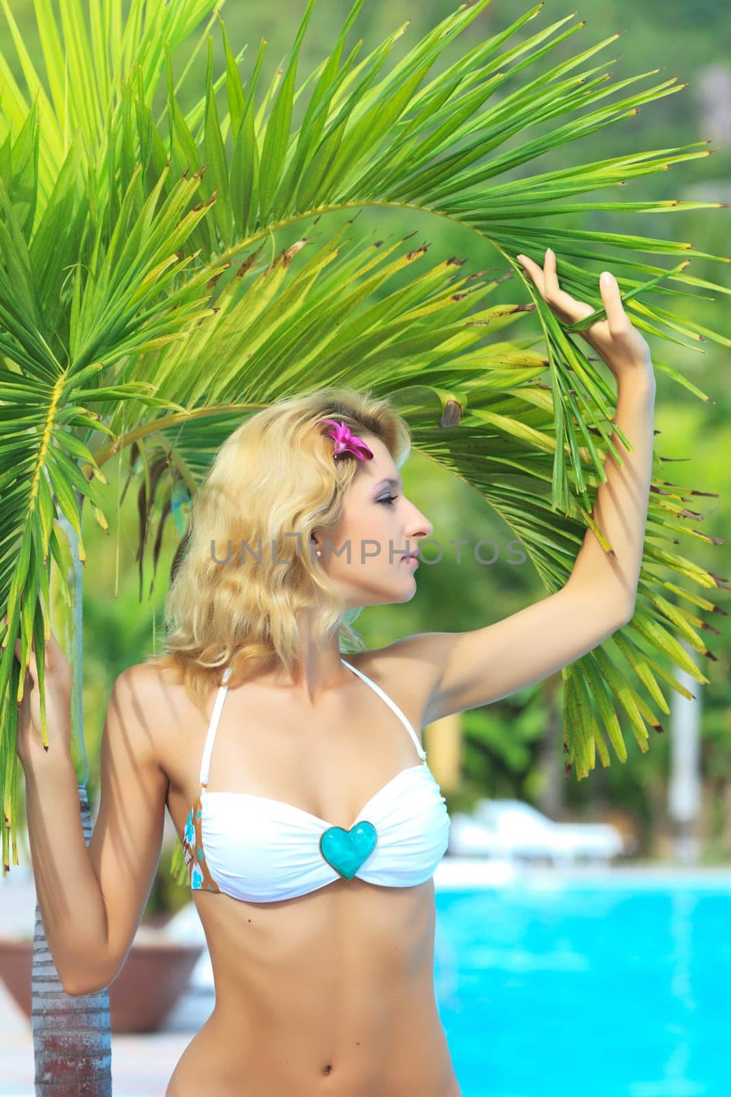 Beautiful woman near swimming pool under palm tree