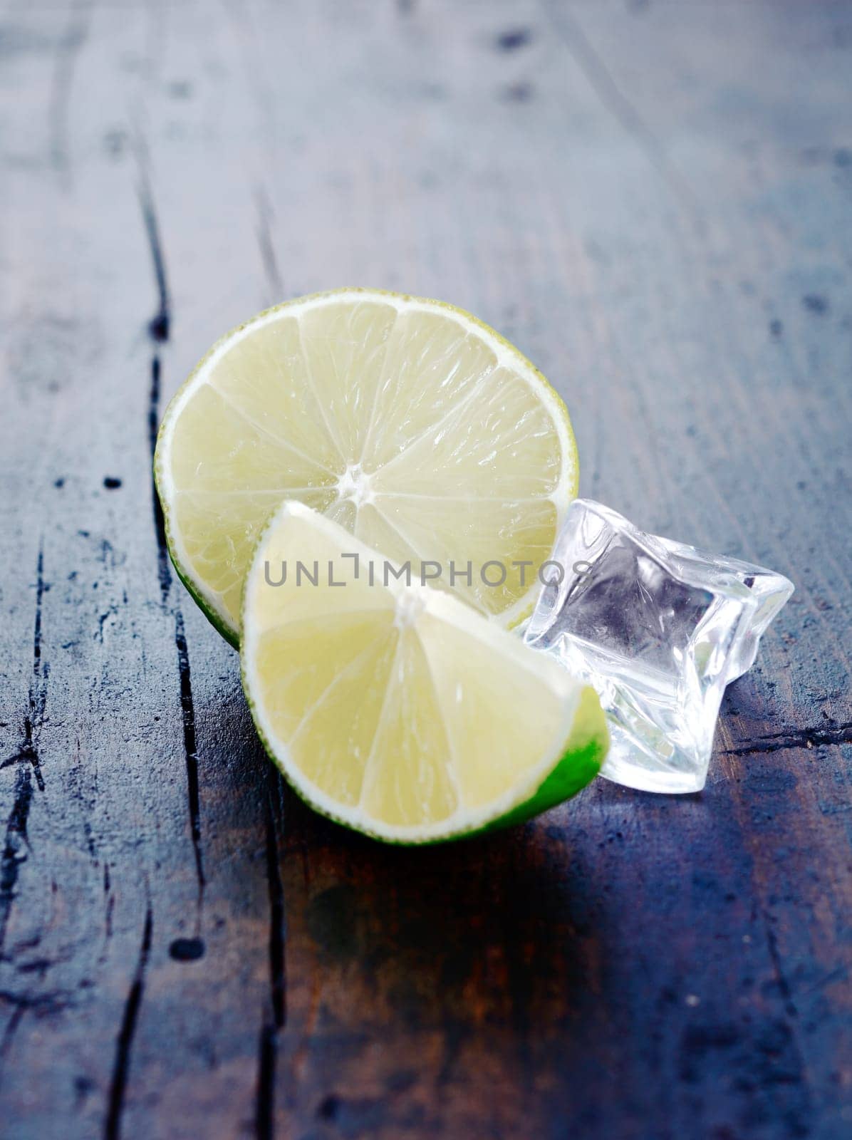 Two Limes with an ice cube on a wooden, ancient background for Drink and Cocktail, especially Caipirinha and Mojito concepts.