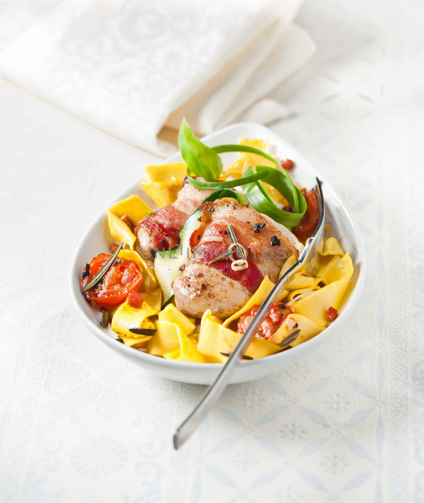 Roasted Chicken wrapped in bacon and pasta Tagliatelle on a white napkin for italian or european food concepts. Maybe for restaurants or menu cards