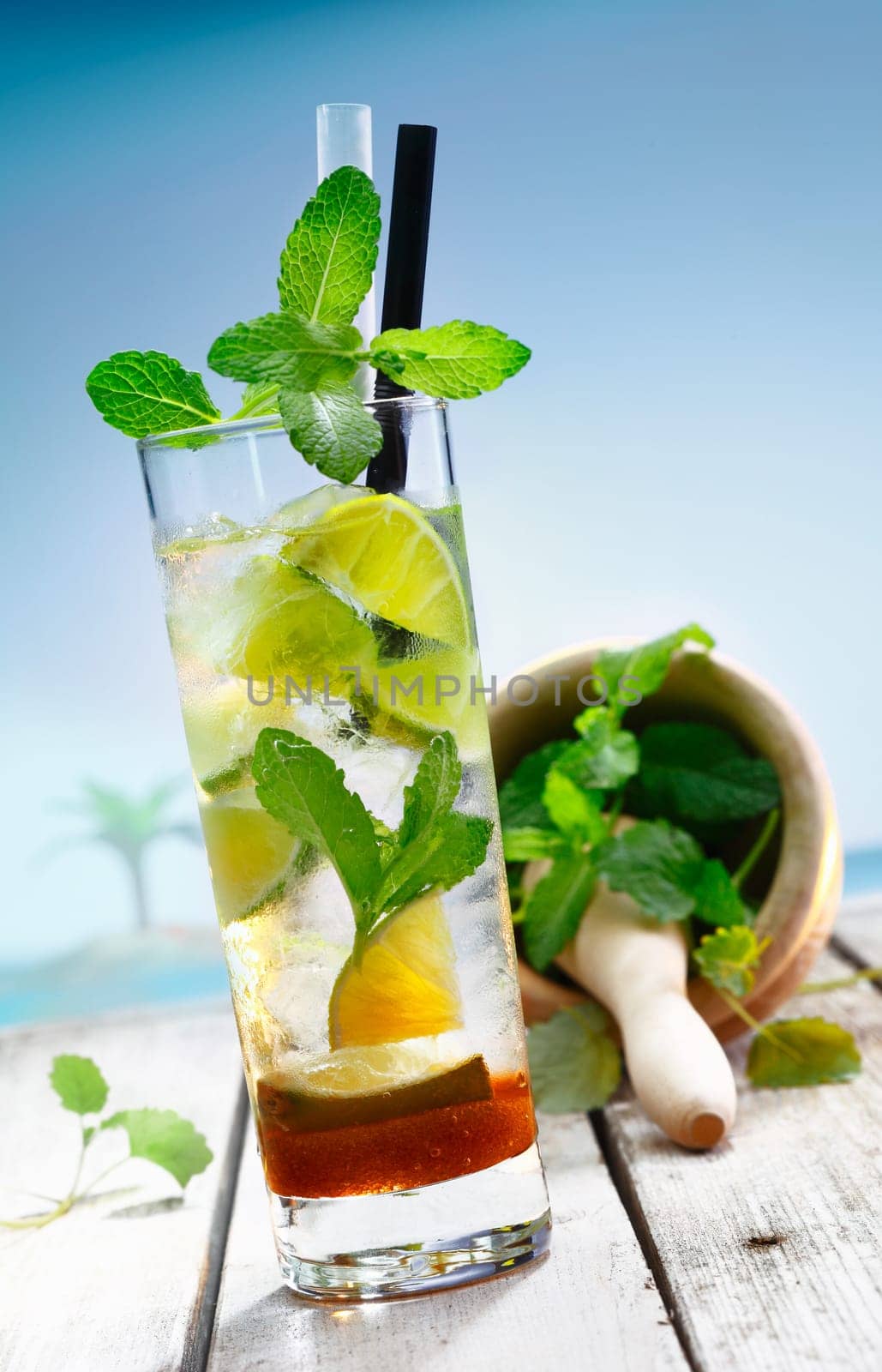 Beach Cocktail with pestle and mortar standing on a jetty in front of a blue lagoon with a palm.