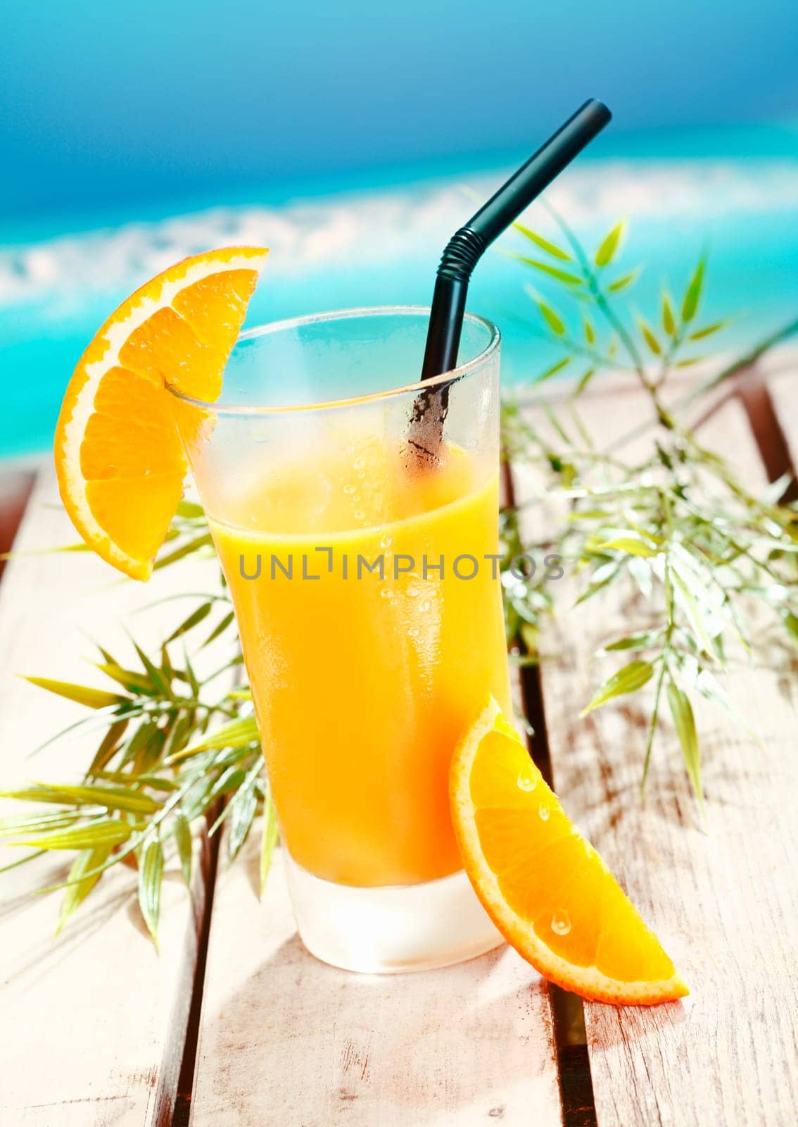 Colourful glass of cold refreshing freshly squeezed orange juice on a wooden deck alongside the ocean at a tropical resort