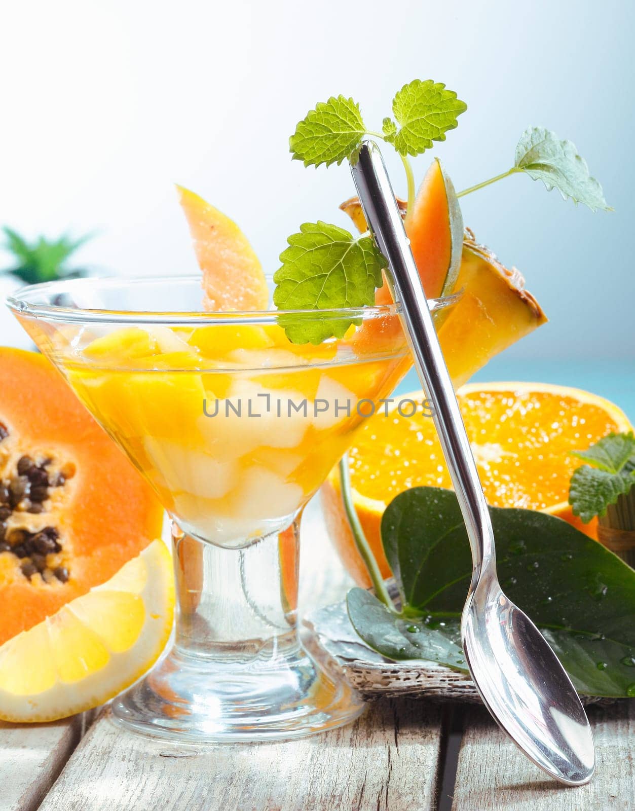 Serving of fresh tropical fruit salad in a conical glass with a spoon and exotic fruits