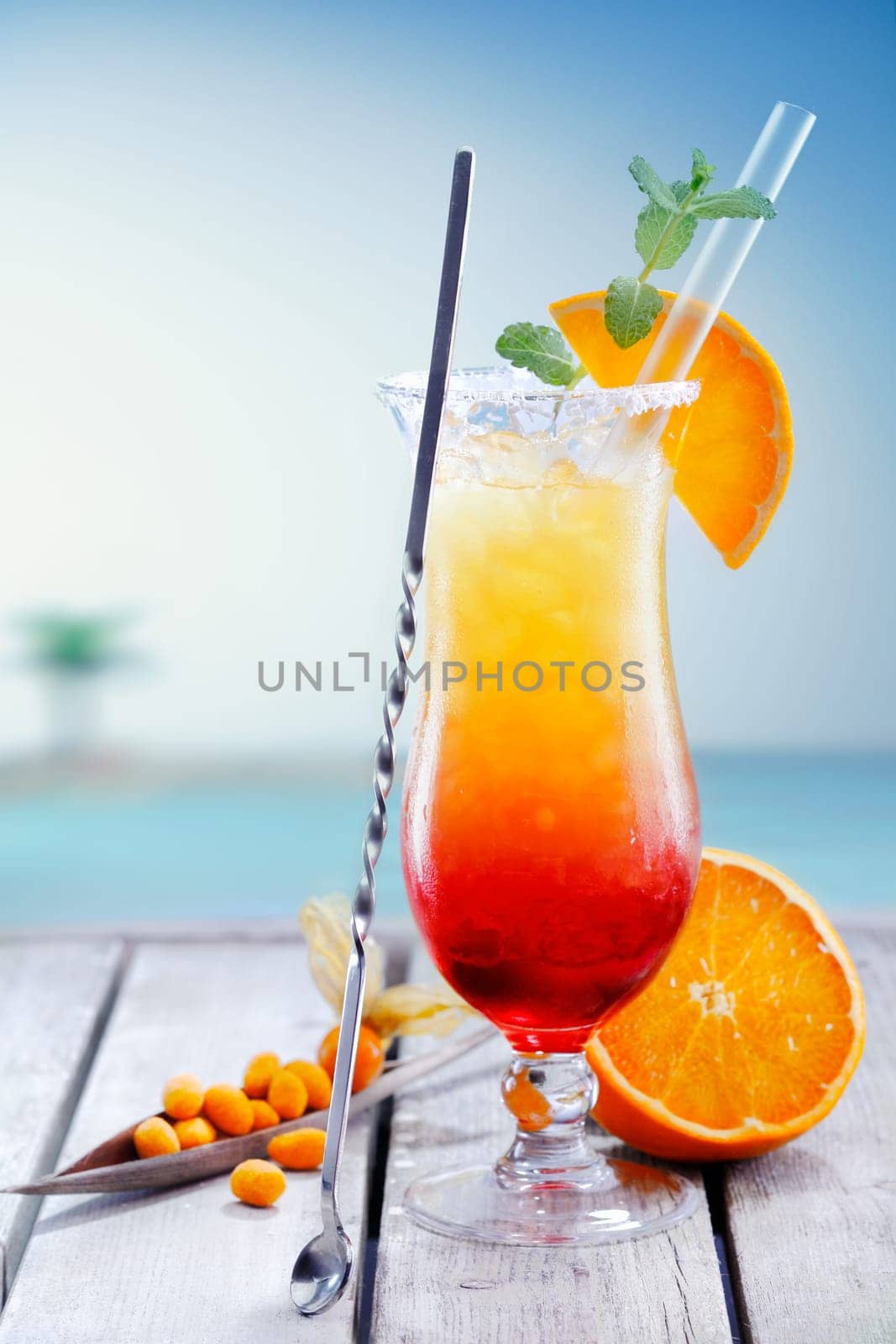 Colourful exotic Tequila Sunrise cocktail served on the rocks with crushed ice and a swizzle spoon