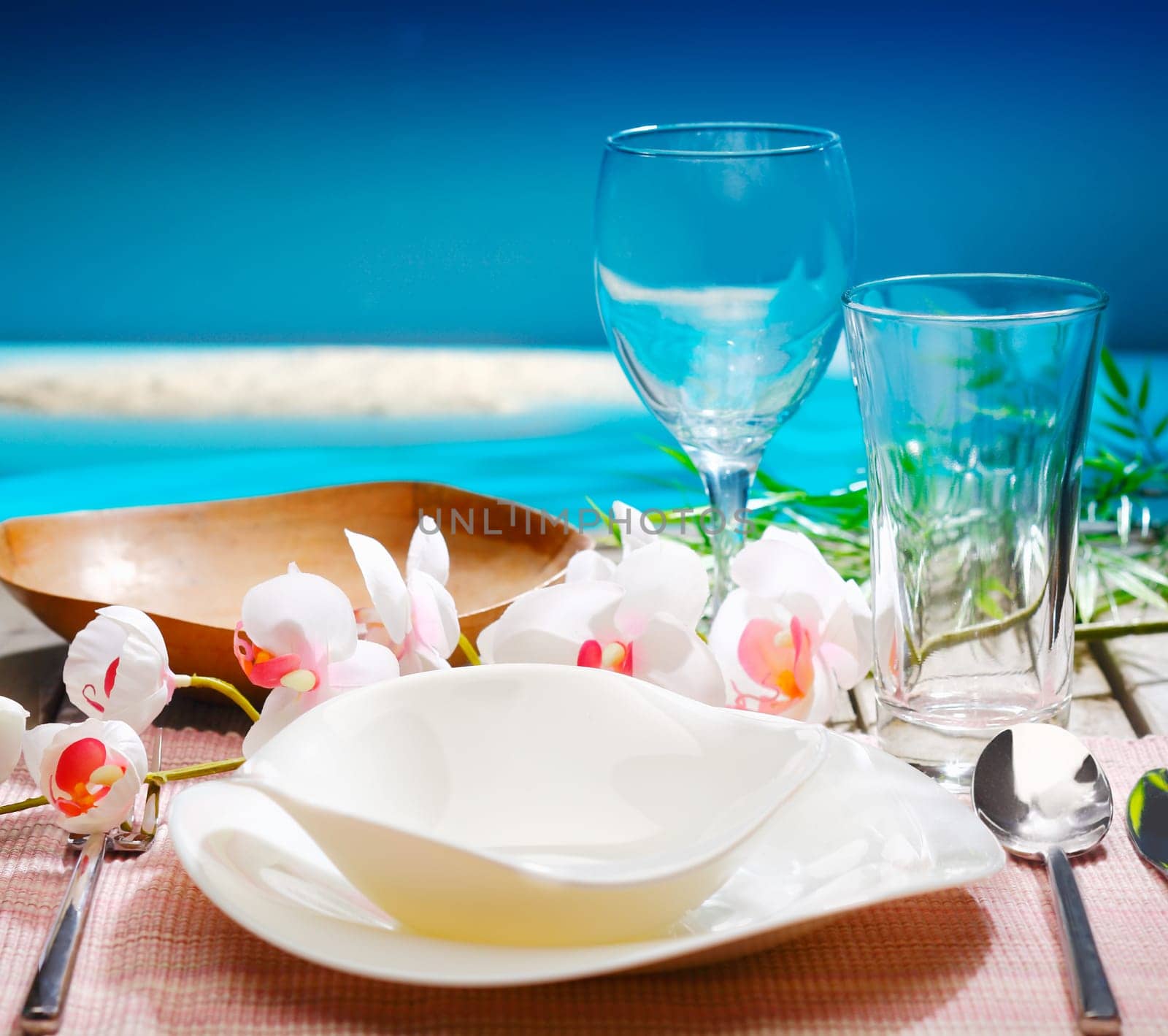 Decorative tropical table setting with stylish dinnerware and orchids overlooking the ocean at a resort restaurant