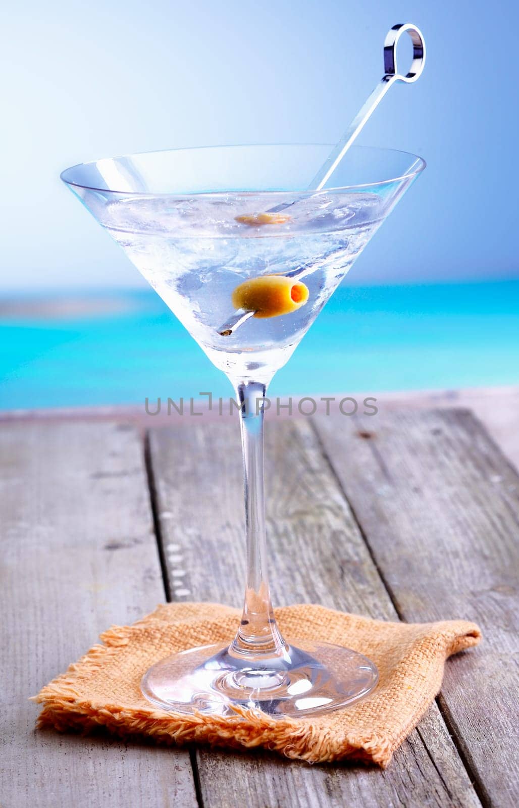 Refreshing martini cocktail in a conical glass with olive garnish served on a summer deck overlooking the ocean