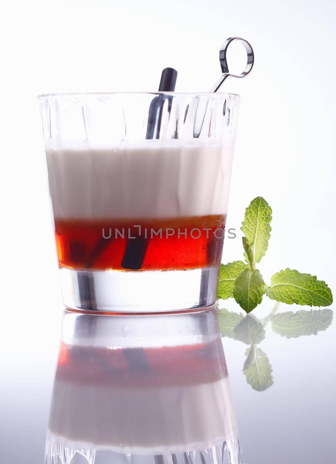 Low angle view of a layered alcoholic cocktail in a tumbler with reflection, background graduating white to grey