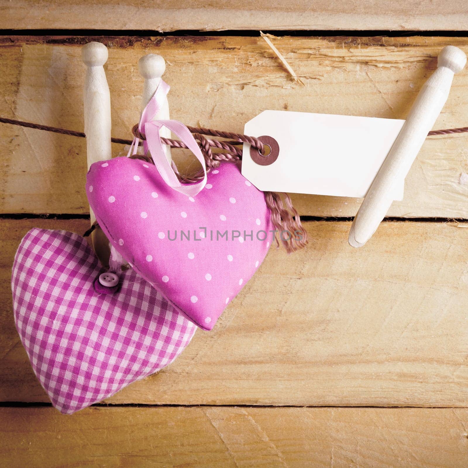 Two romantic pink patterned textile hearts hanging from rustic wooden pegs with a blank label