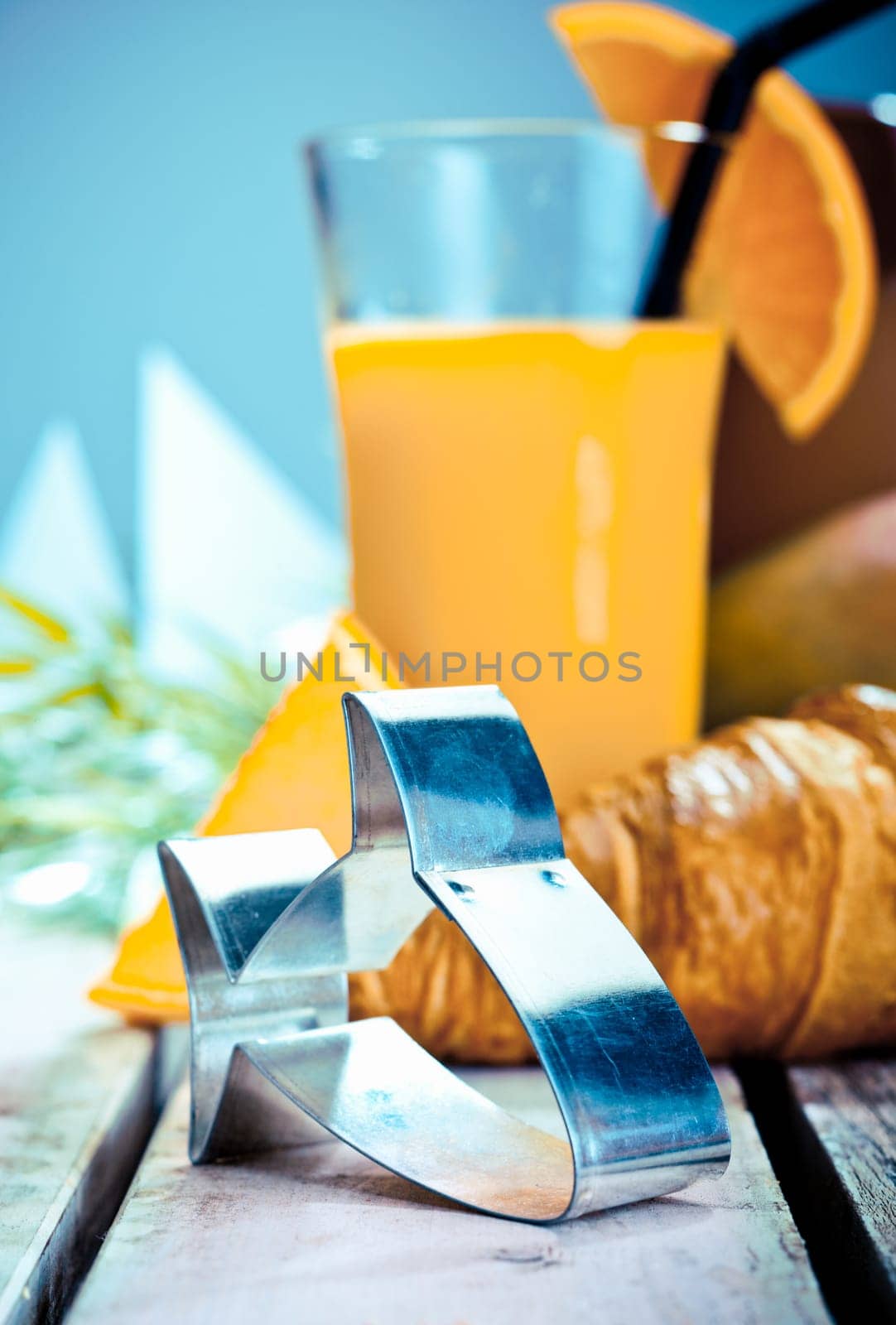 Tropical catering still life with focus to a stylised fish cookie cutter with fresh orange cocktail and croissant background against blue sky