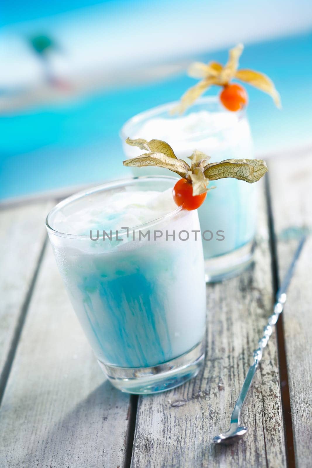 Two glasses of blended blue cold curacao cocktail on a deck overlooking the sea at a tropical resort