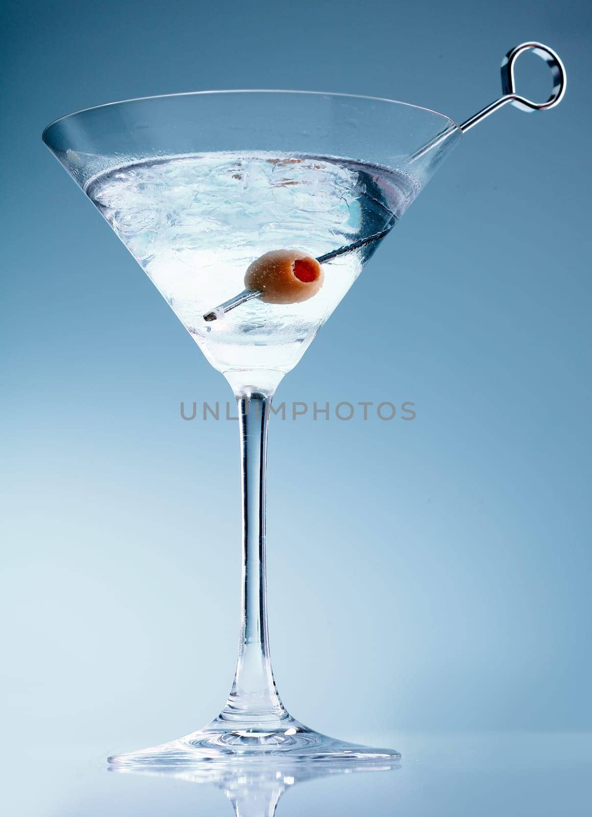 Shaken martini cocktail in a conical glass with an olive on a suffused soft blue background
