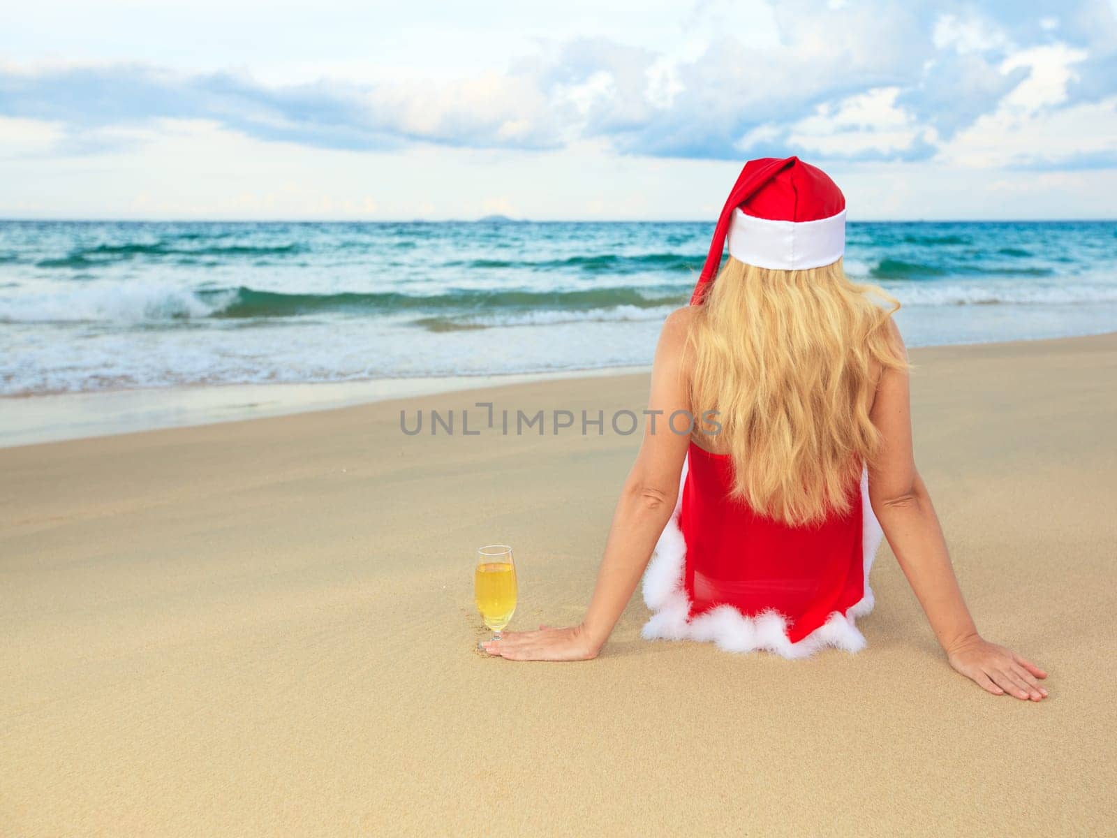 Miss Santa sitting near the ocean with glass of wine