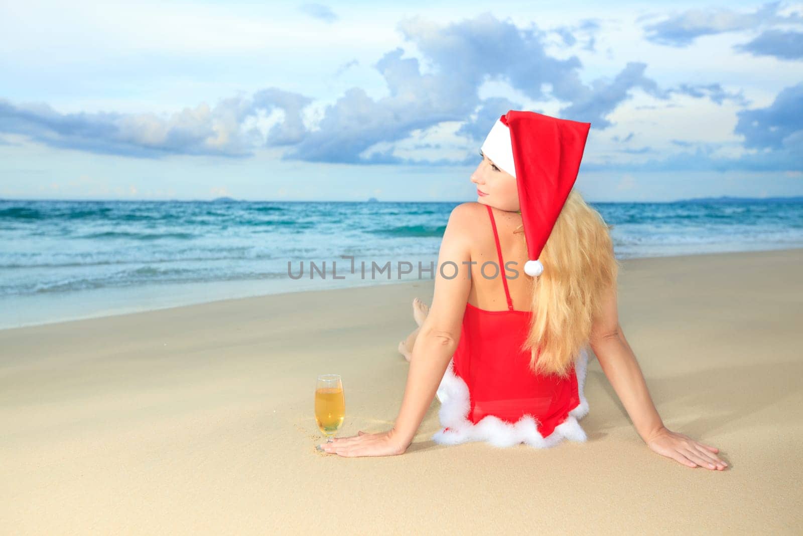 Miss Santa sitting near the ocean with glass of wine
