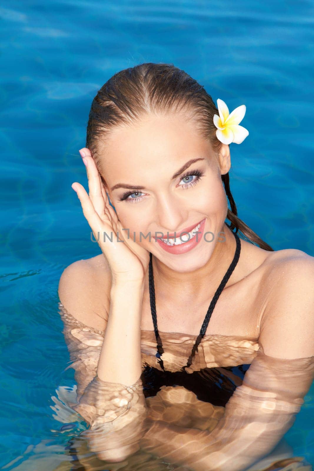 Smiling tropical beauty in a bikini and with a frangipani flower in her wet hair relaxing in sparkling pool