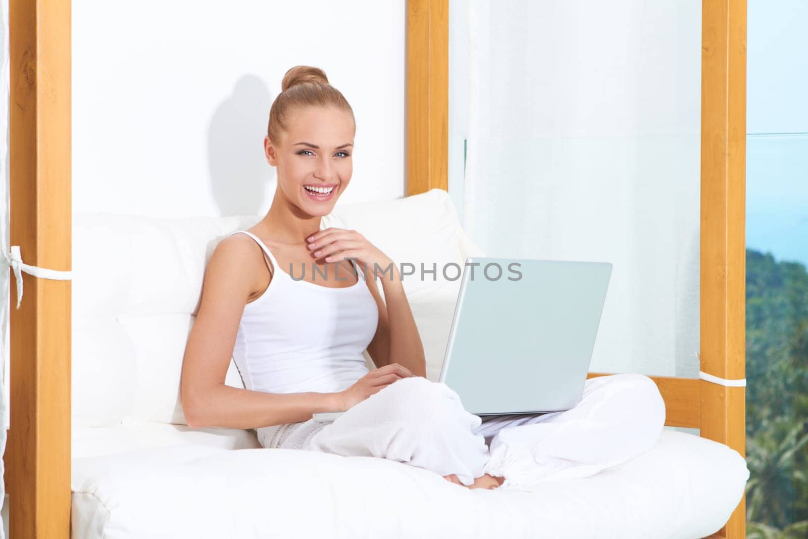 Joyful woman seated on white cushions laughing with with her laptop balanced on her crossed legs