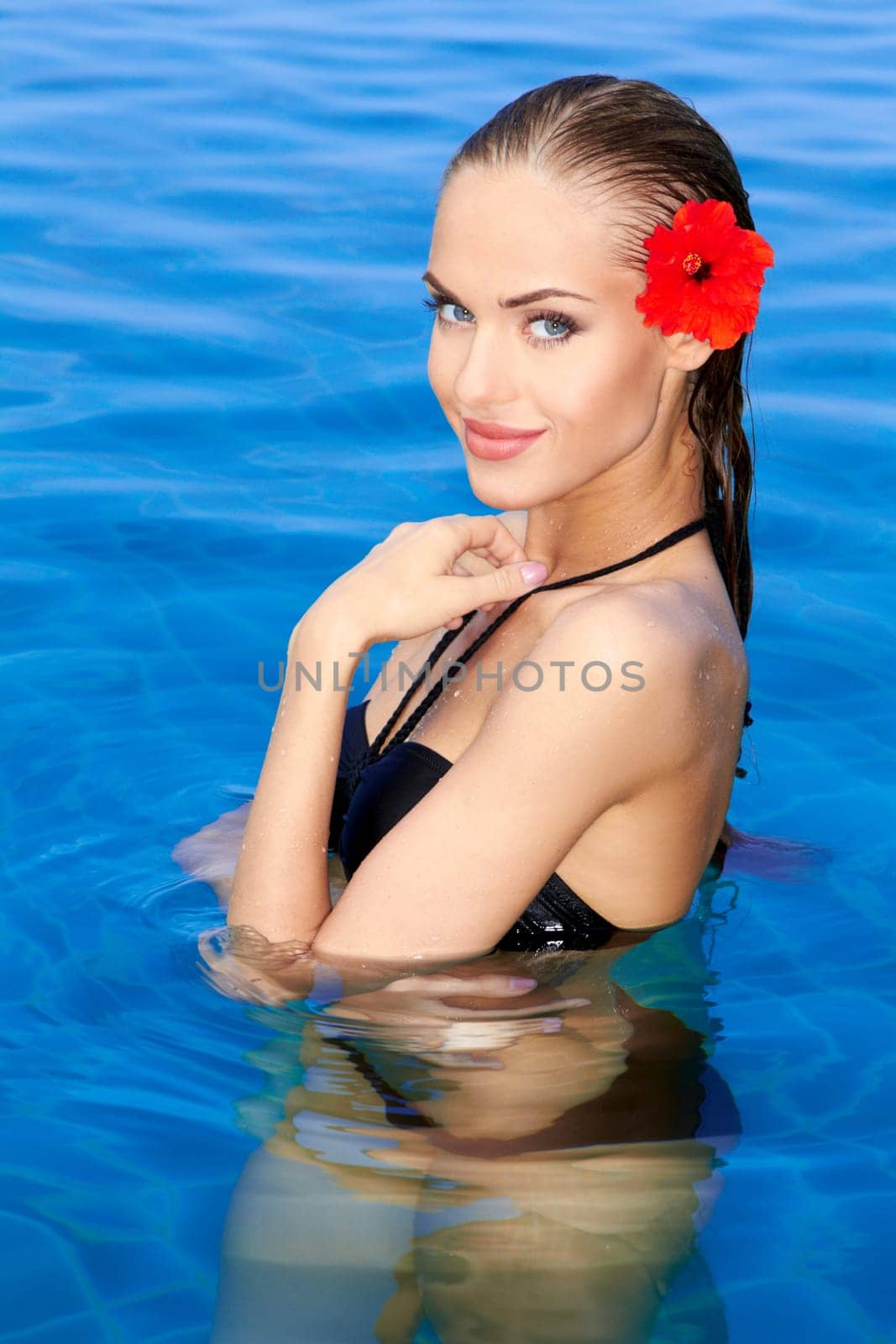 Tropical girl with flower on her ear posing in swimming pool