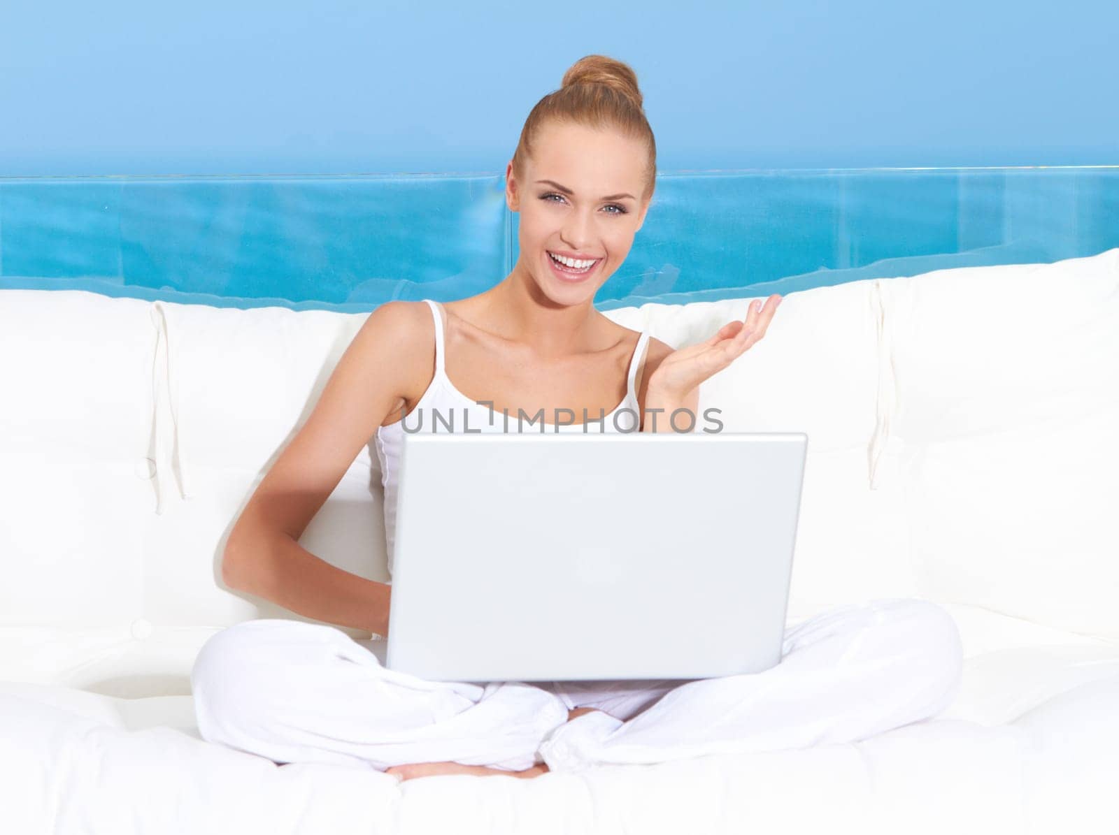 Fresh bright portrait of a woman sitting cross legged on a canopied seat with her laptop backed by a large window overlooking the ocean