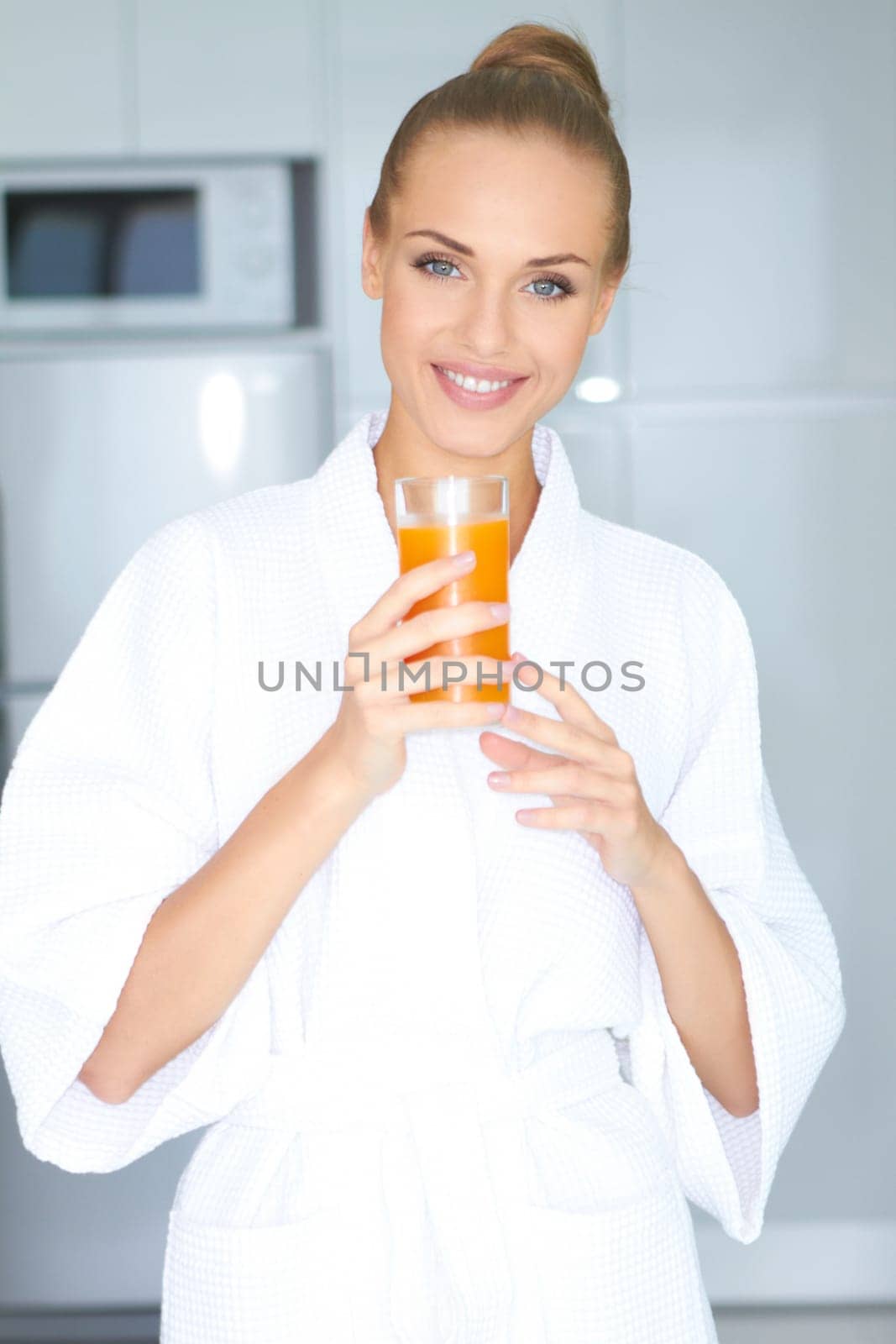 Beautiful elegant woman in a white bath robe drinking a large glass of fresh orange juice