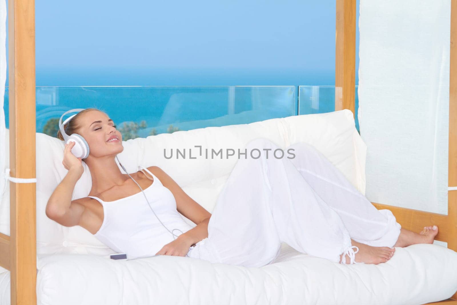 Dreaming woman wearing headphones relaxing on a white sofa listening to music