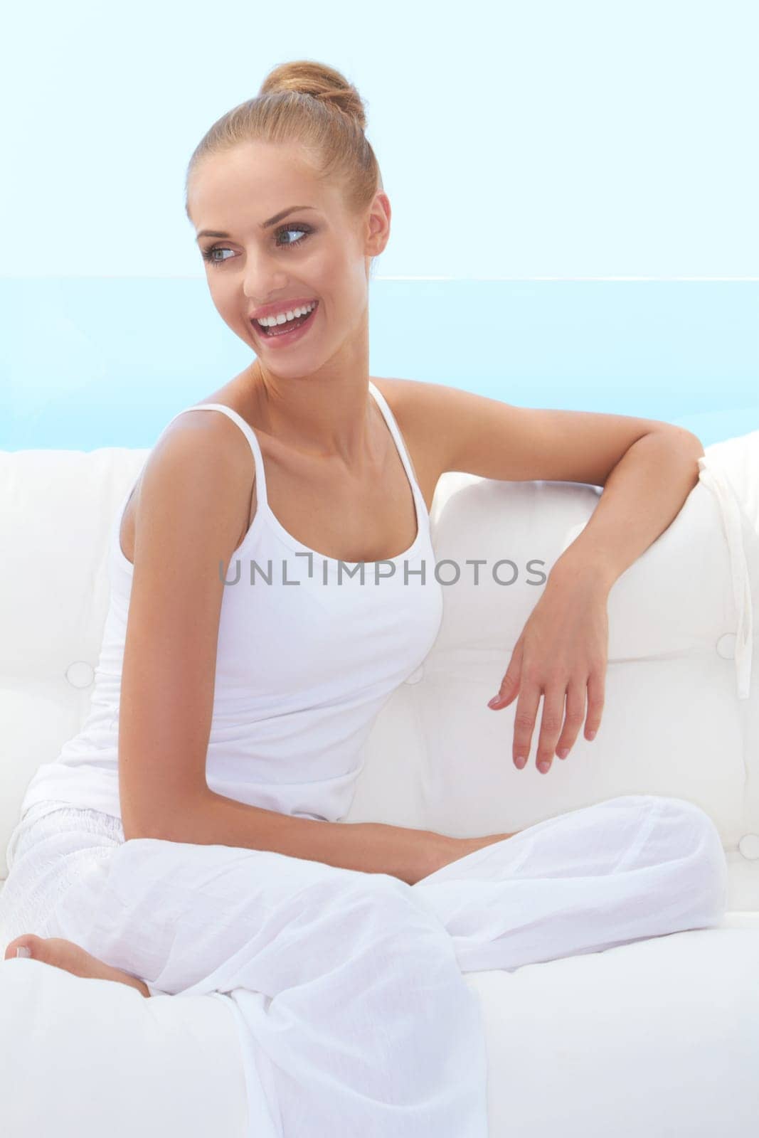 Happy confident beautiful woman smiling broadly and looking off camera while seated on a white couch