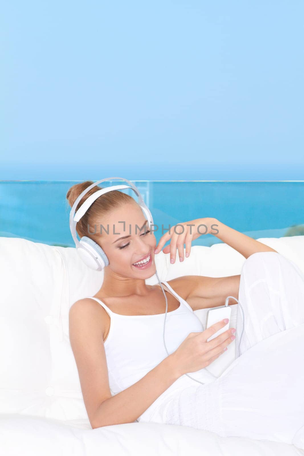 Cute woman wearing headphones relaxing on a white sofa listening to music