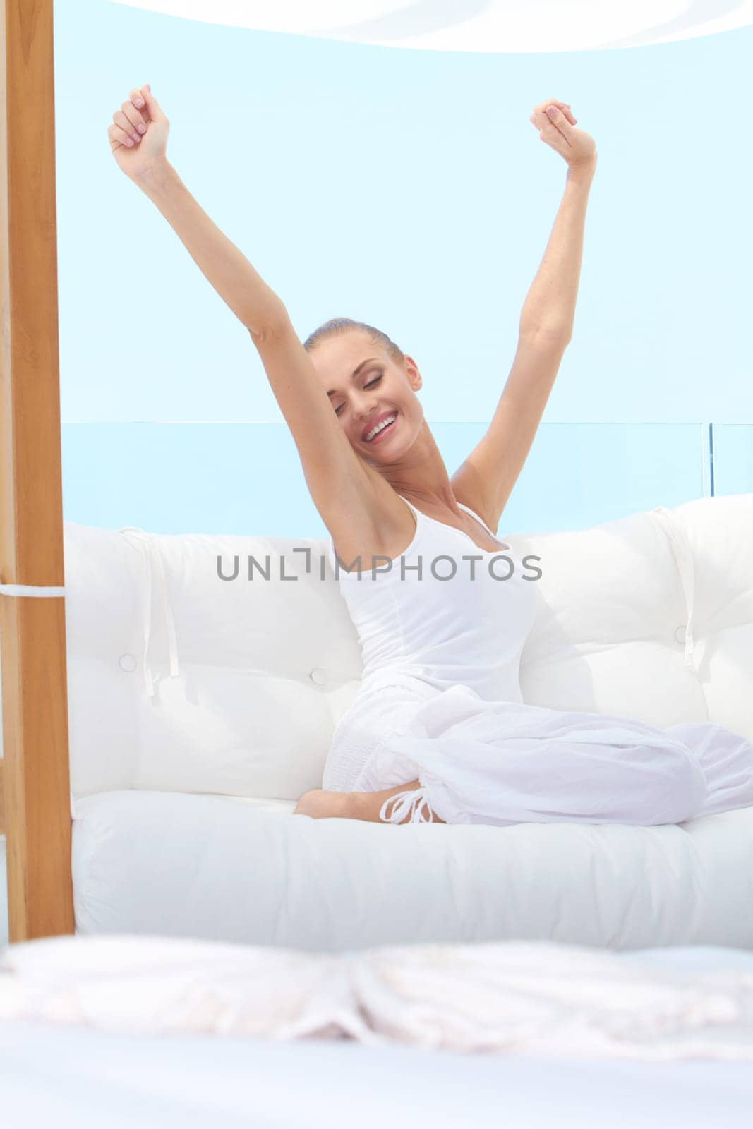 Pretty woman in casual outfit curled up on a white window seat stretching languidly in the warm sunshine