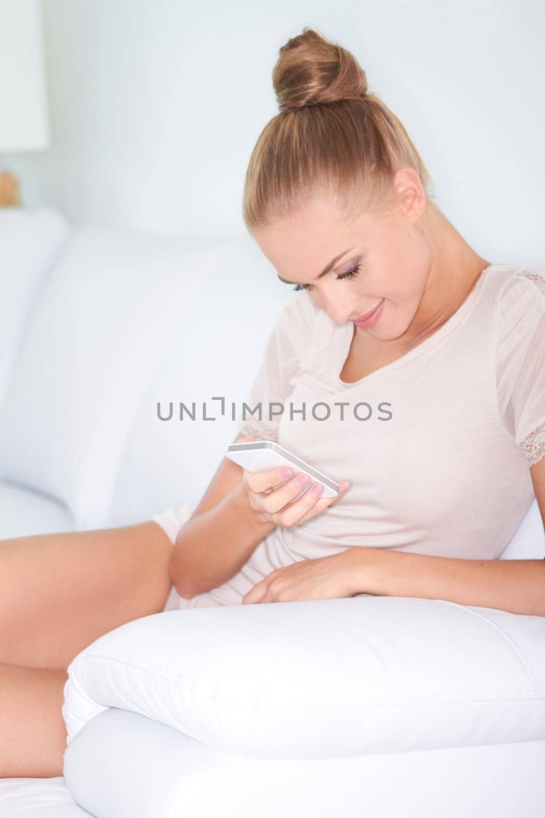 Beautiful woman reclining on a white sofa texting on her mobile phone