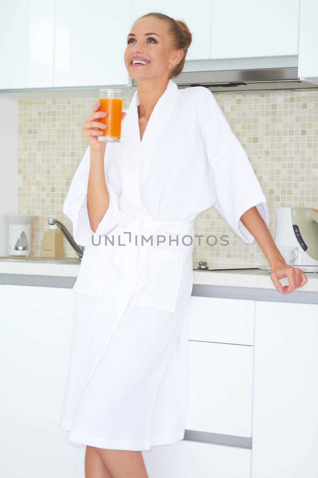 Glamorous woman in a white bath robe enjoying a large glass of fresh orange juice for breakfast