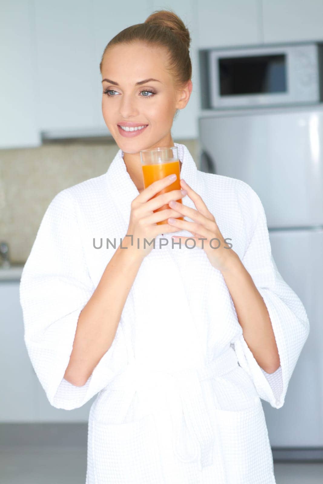 Stylish woman in a thick white towelling gown drinking a large glass of healthy orange juice