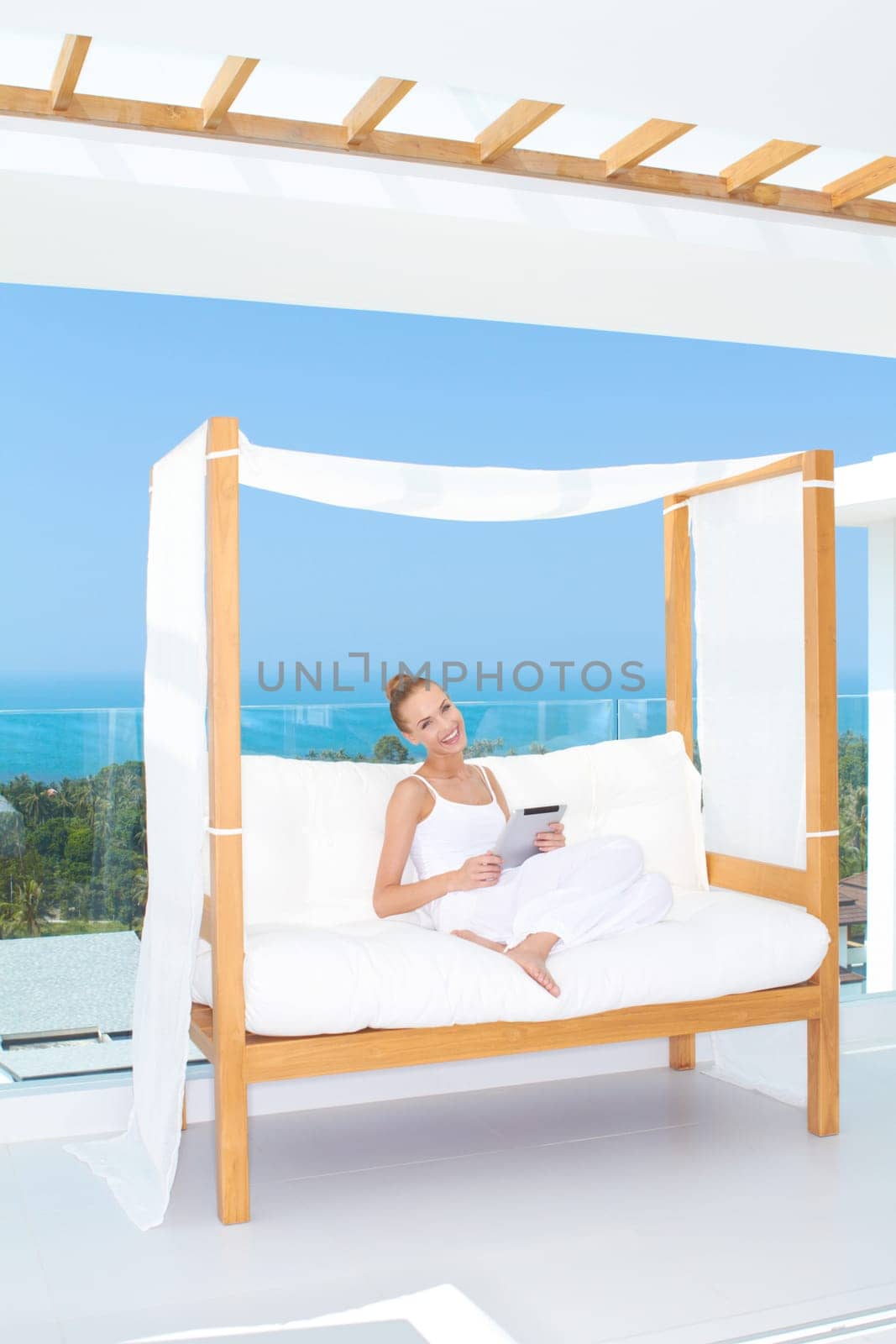 Fresh high key image of a beautiful woman wearing a white outfit relaxing on a white couch using a touchpad notebook