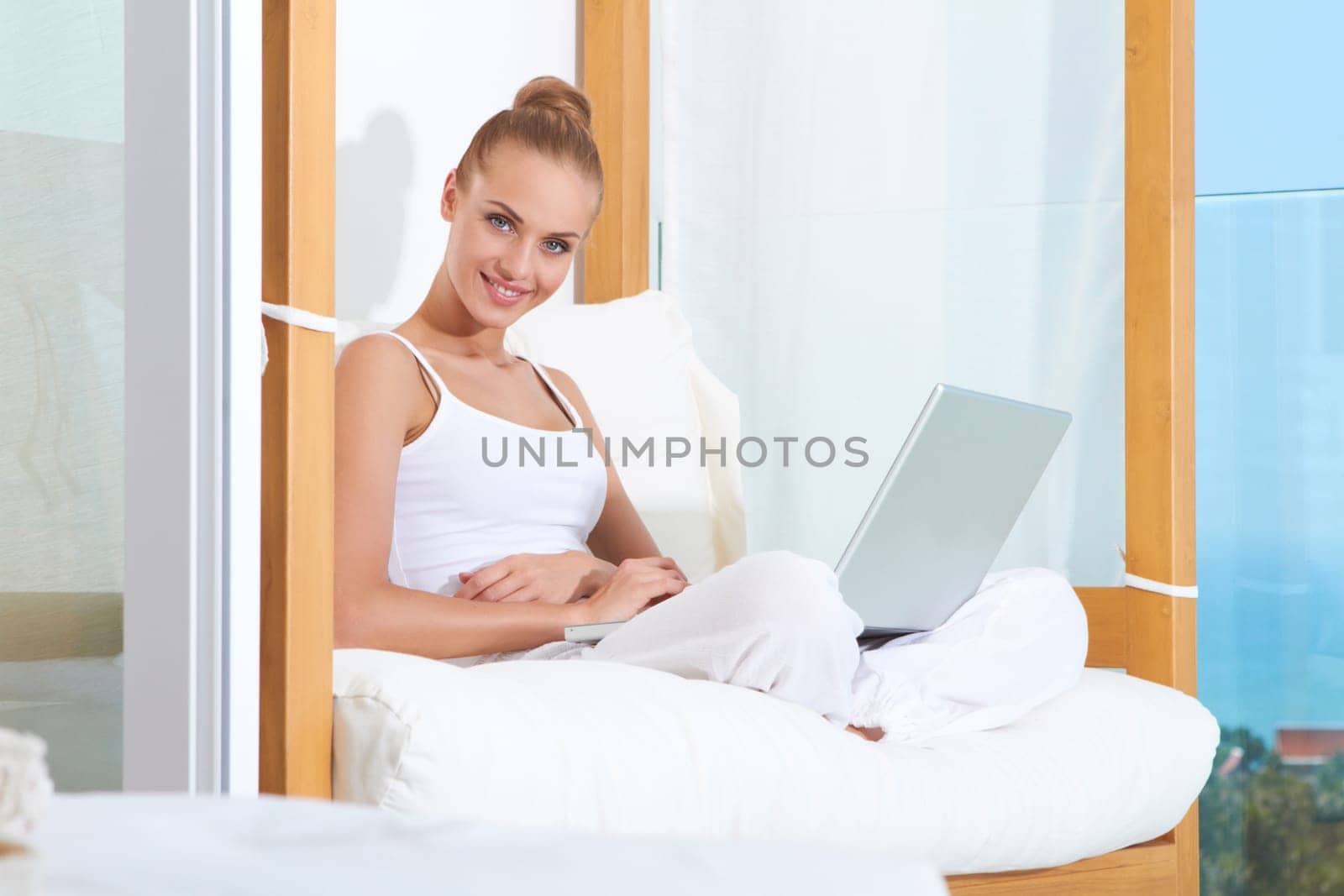 Joyful woman seated on white cushions laughing with with her laptop balanced on her crossed legs