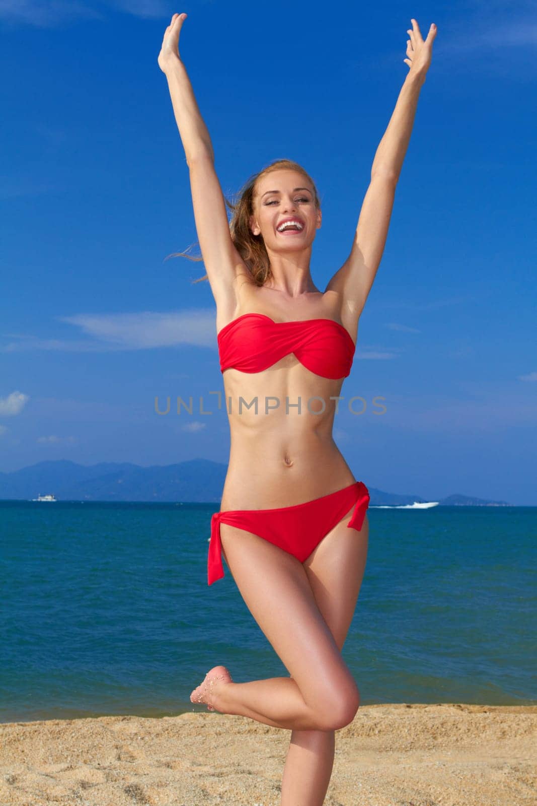 Joyful woman in red bikini with arms raised posing by the sea
