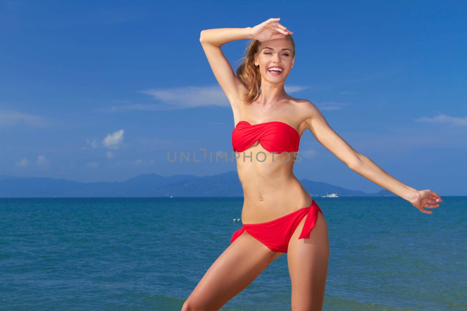 Beautiful laughing shapely woman on summer vacation posing in front of the ocean in her red bikini