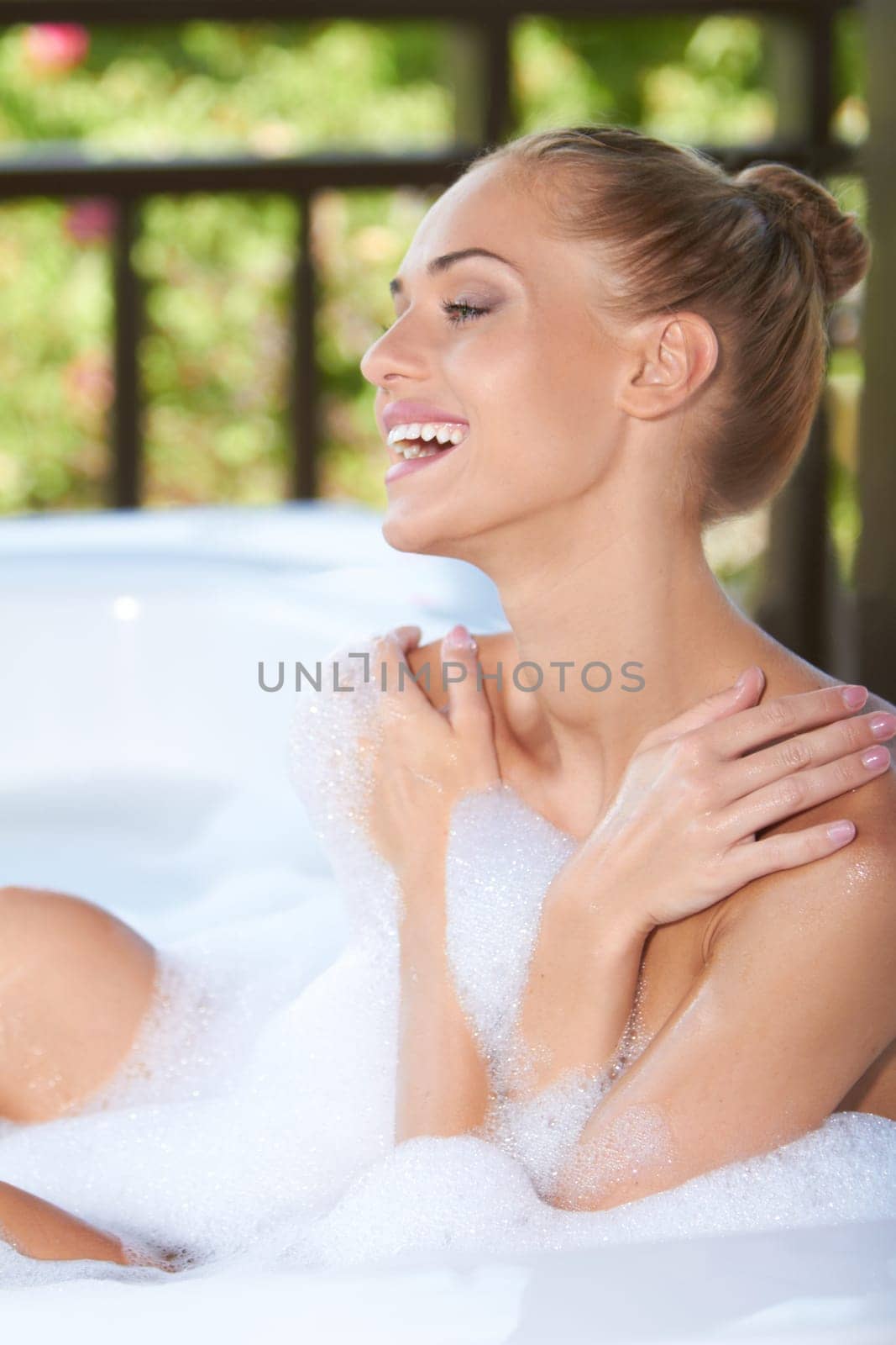 Vivacious blonde woman laughing in enjoyment as she soaks in the soapy bubbles of her bubble bath