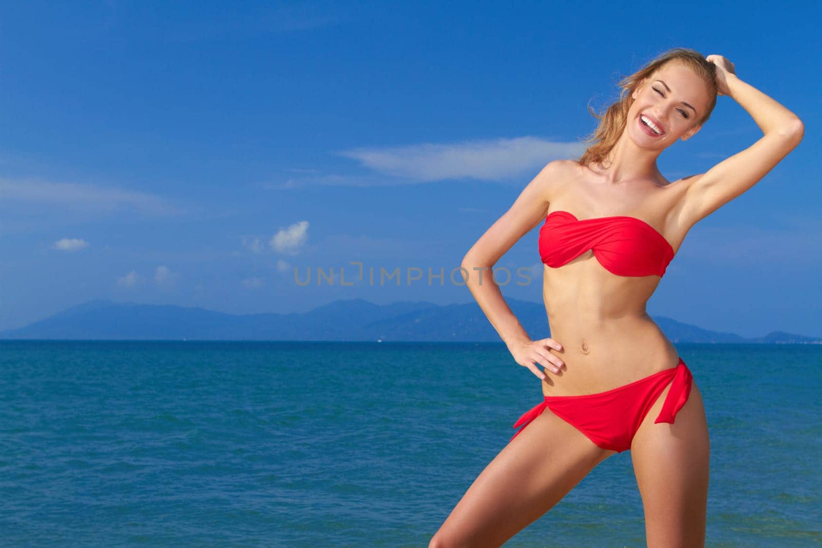Beautiful smiling woman posing in red bikini with blue sea and sky as a background
