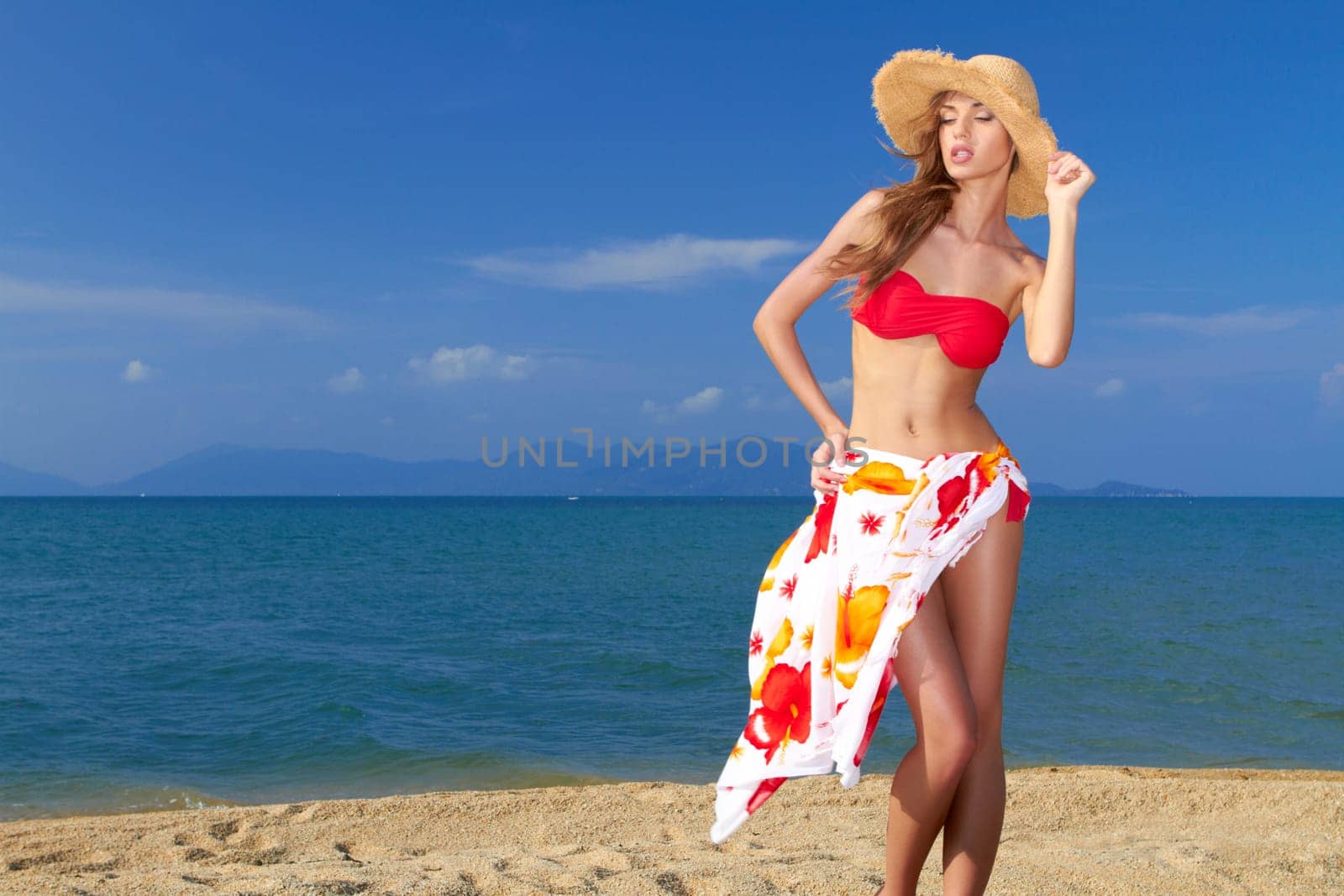 Coy blonde beauty in a red bikini showing her beautiful legs and figure