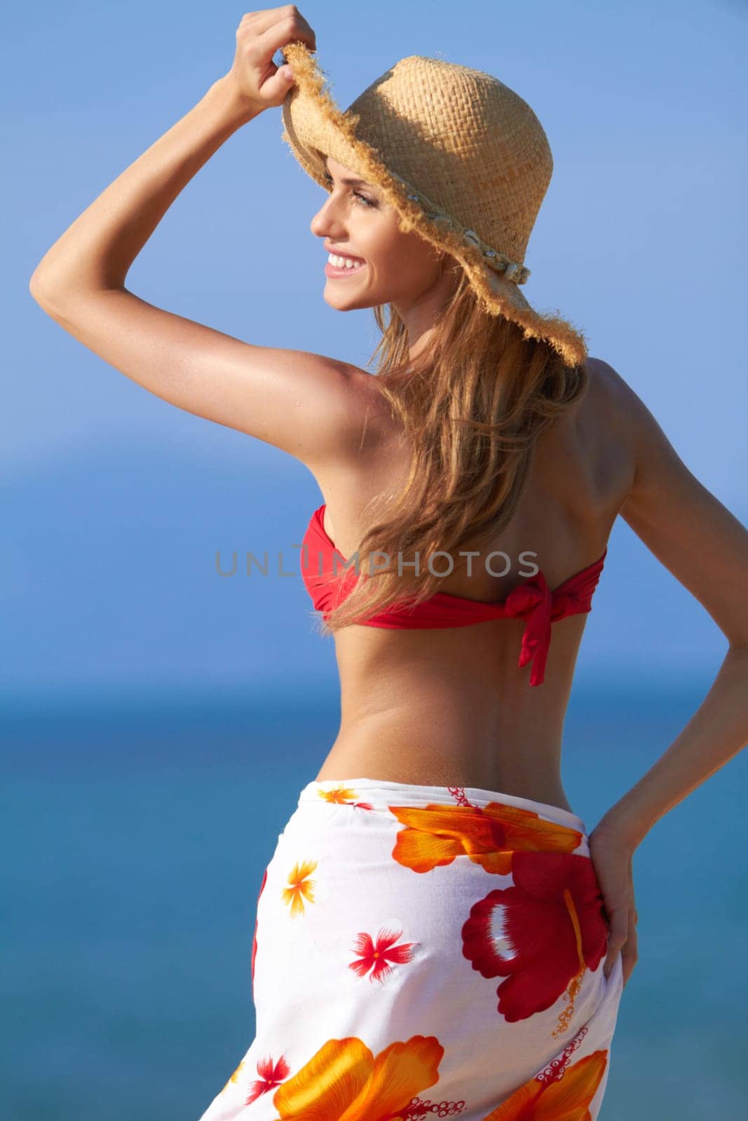 Smiling blonde in a red bikini and sarong wrap with a hat for sun protection