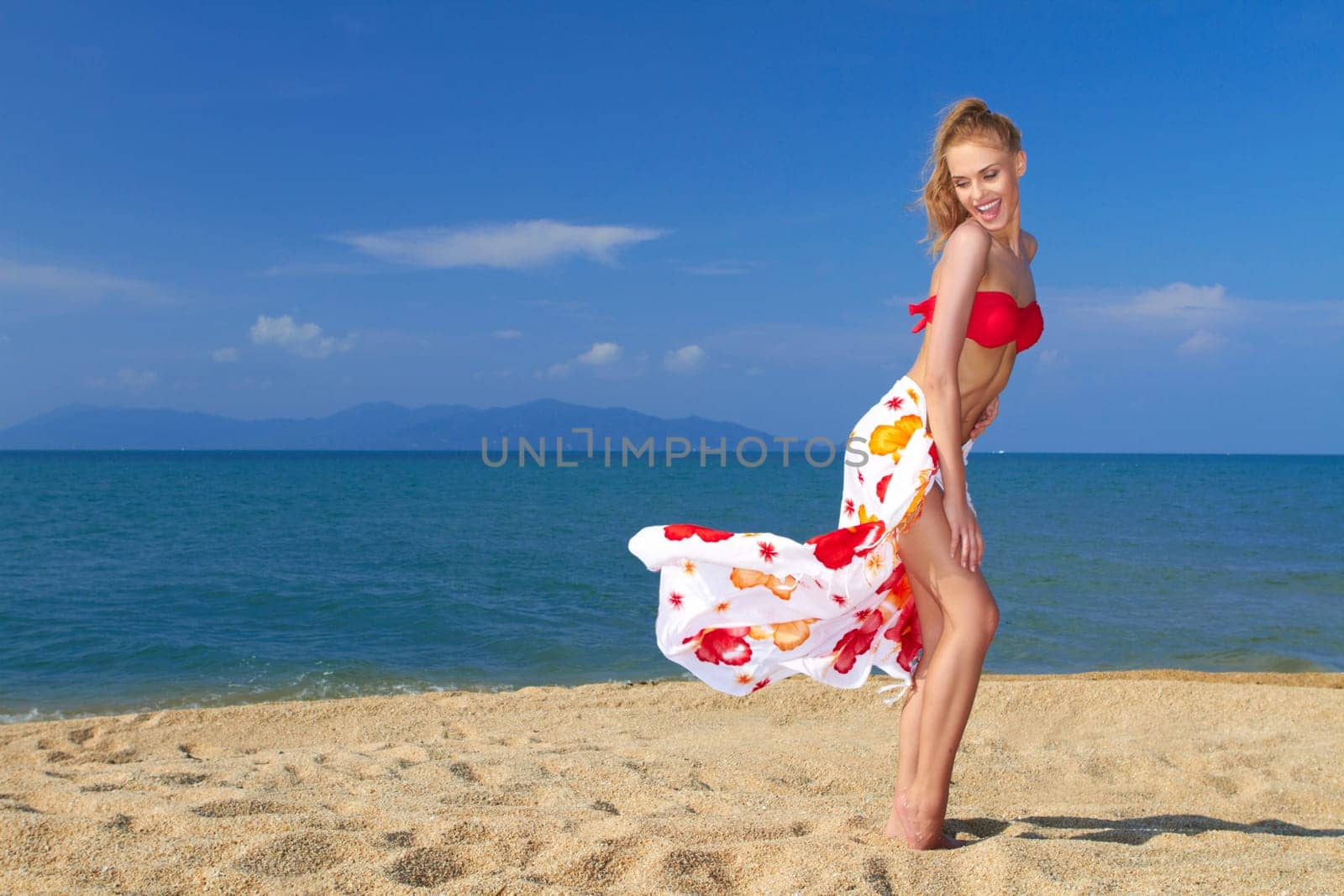 Playful moment with the wind in her sarong entertains a pretty blonde on the beach