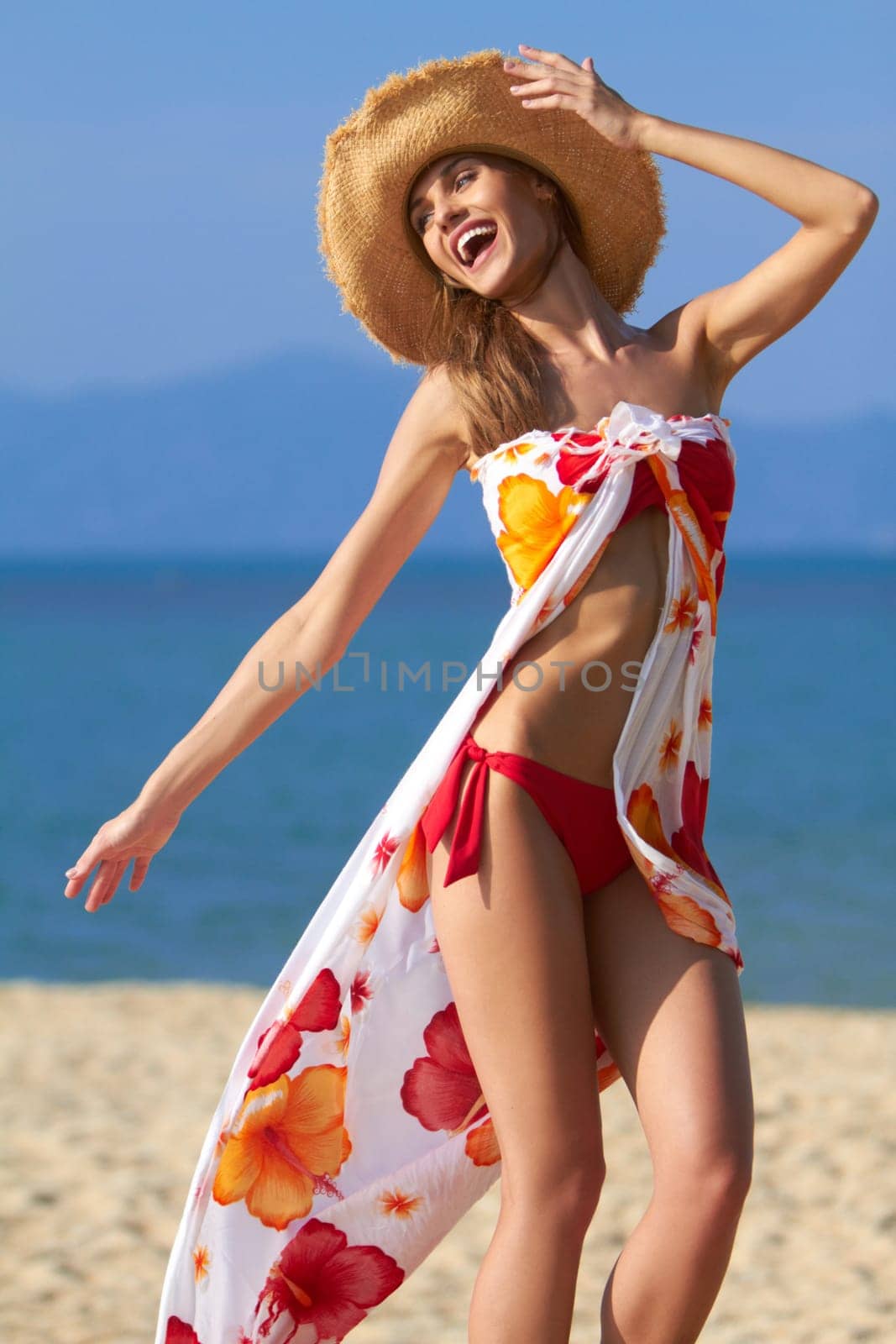 Carefree young woman in a bikini and sarong playing on the beach