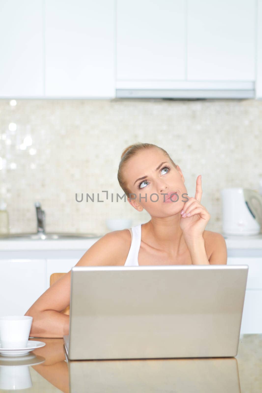 Thinking woman sitting at her laptop computer in her kitchen enjoying something she has just read over the internet