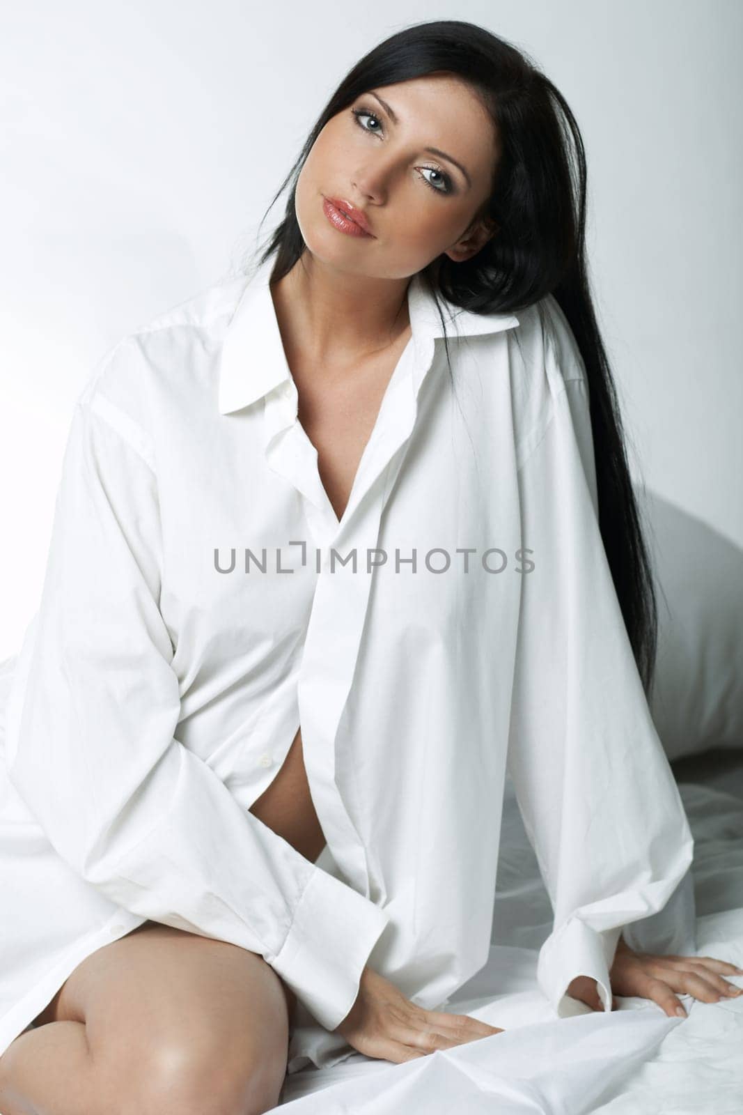 Beautiful brunette woman on bed, wearing white large casual shirt