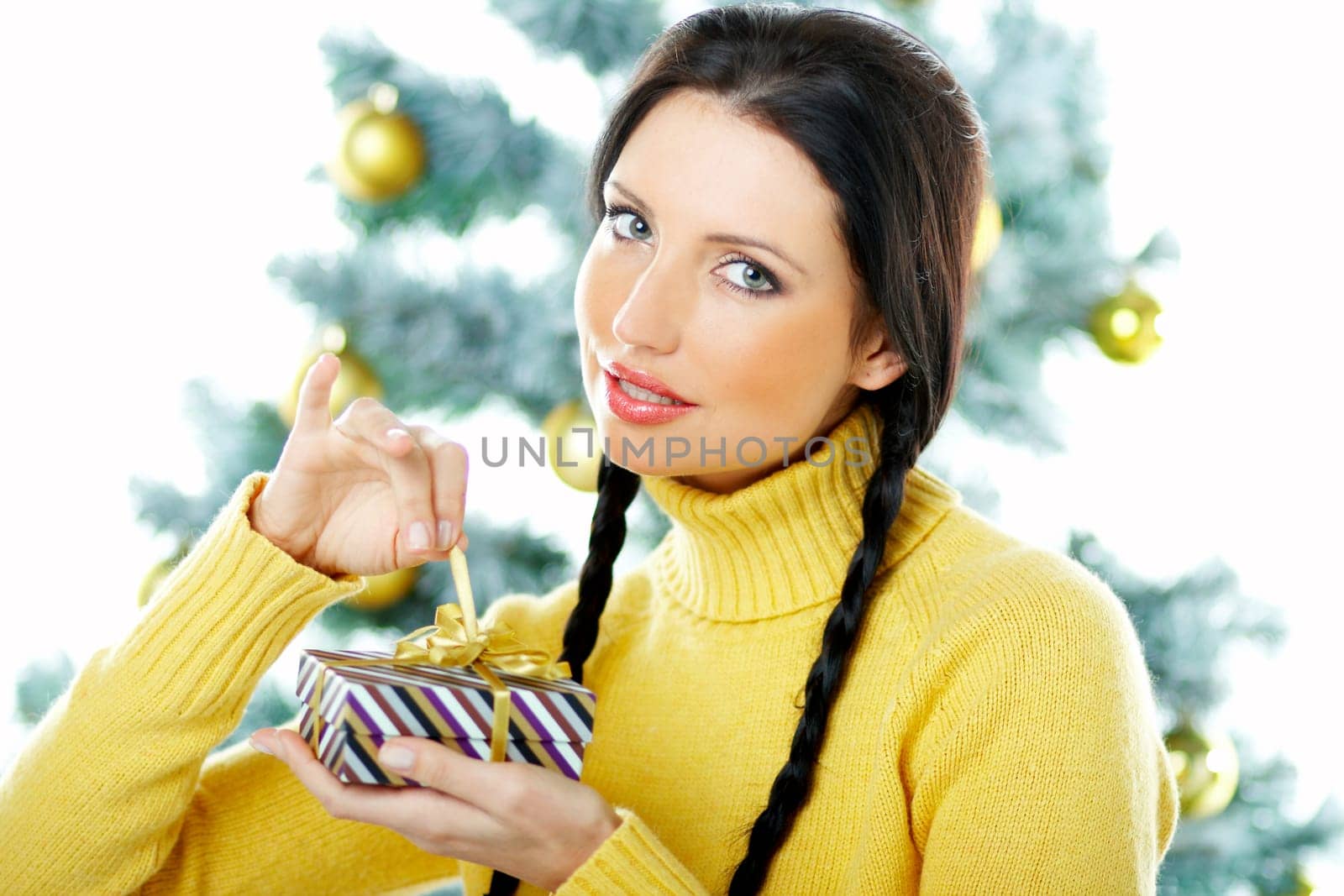 Beautiful brunette woman next to christmas tree on white background holding boxed gift
