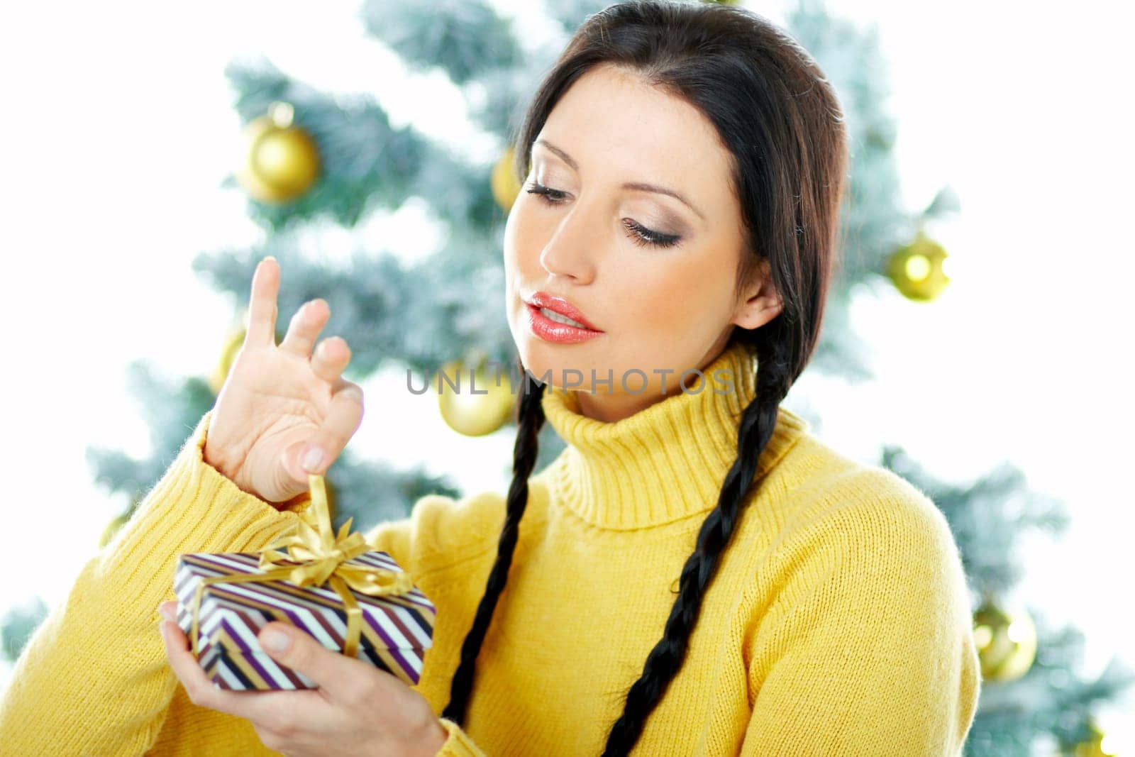 Beautiful brunette woman next to christmas tree on white background holding boxed gift