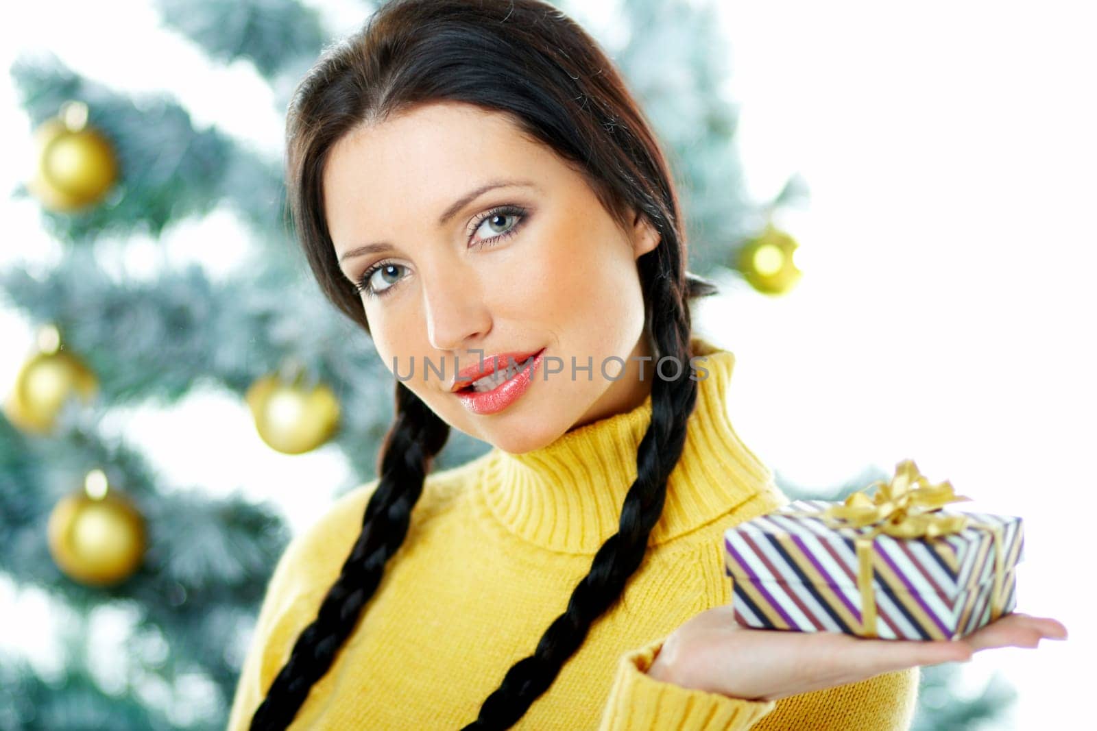 Beautiful brunette woman next to christmas tree on white background holding boxed gift